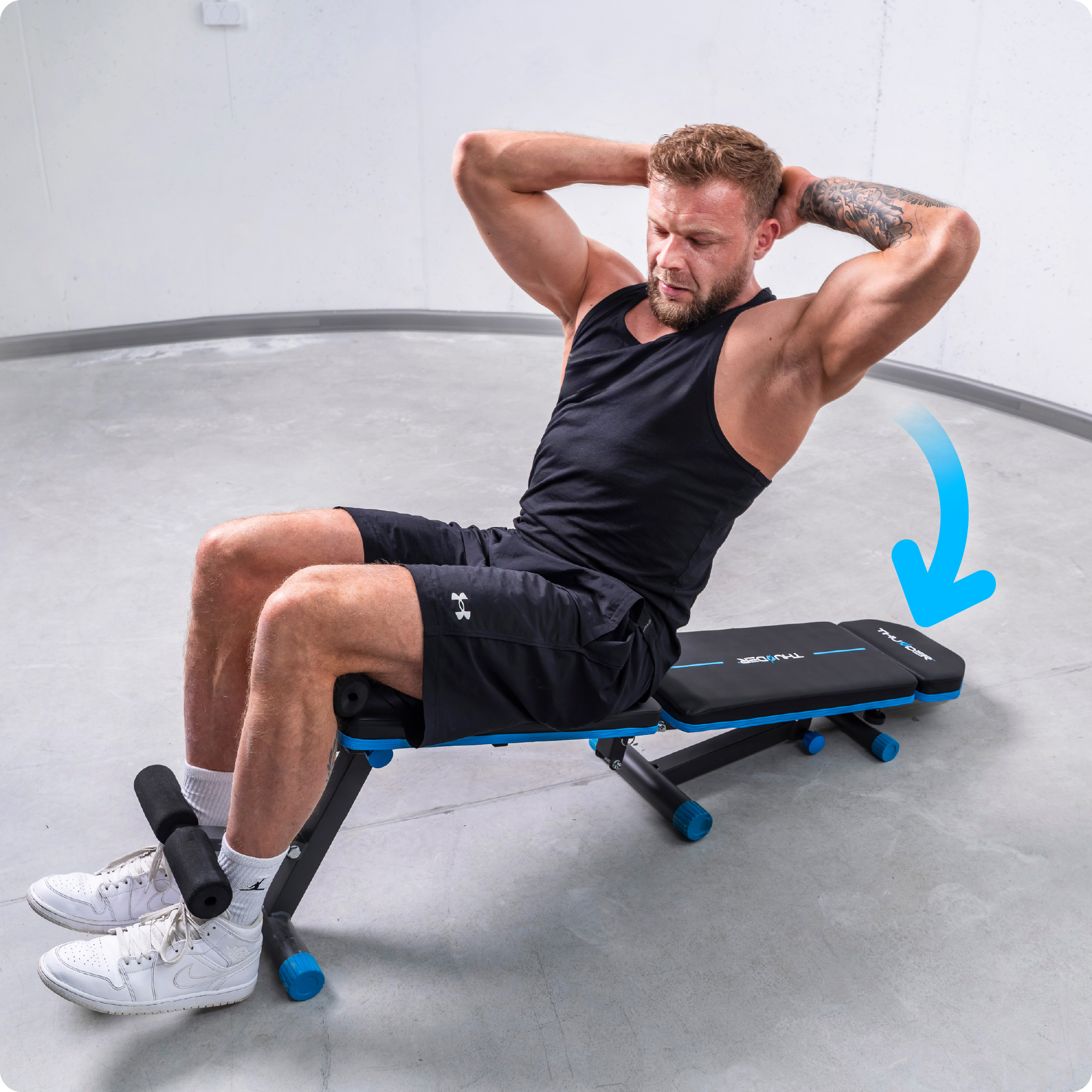 Mężczyzna robi brzuszki na czarno-niebieskiej ławce do ćwiczeń. Ma na sobie czarne szorty i koszulkę.