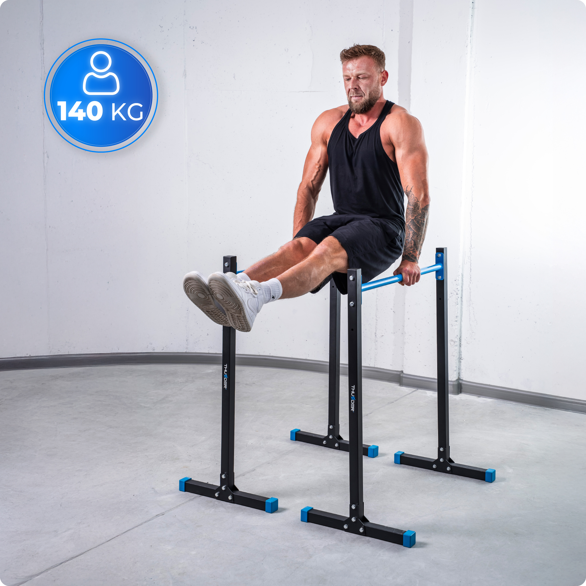 Mężczyzna robi L-sit na poręczach. Czarne szorty, podkoszulek. 140 kg limit wagowy.