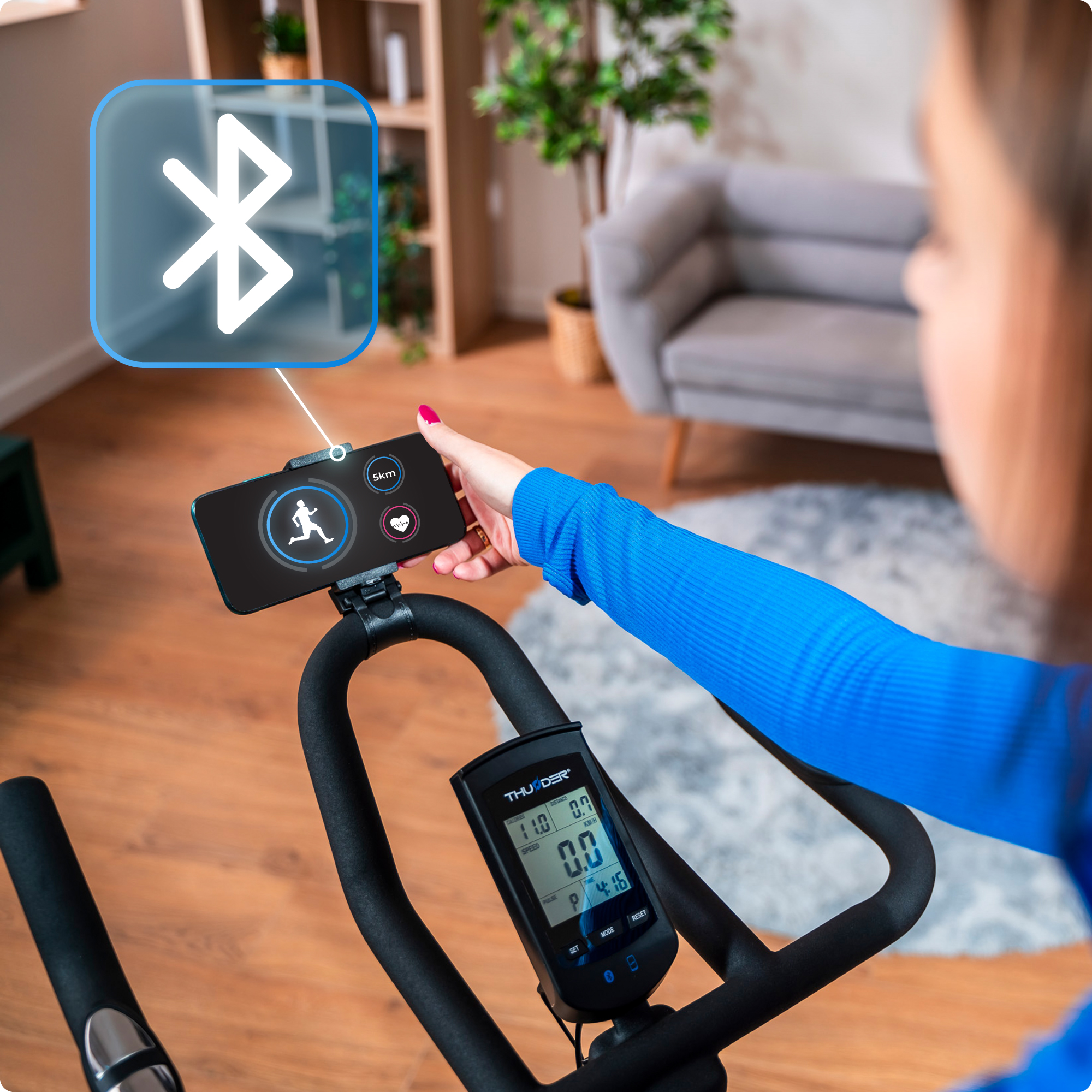 Osoba korzysta z telefonu podłączonego do roweru treningowego. Telefon wyświetla dane treningowe.