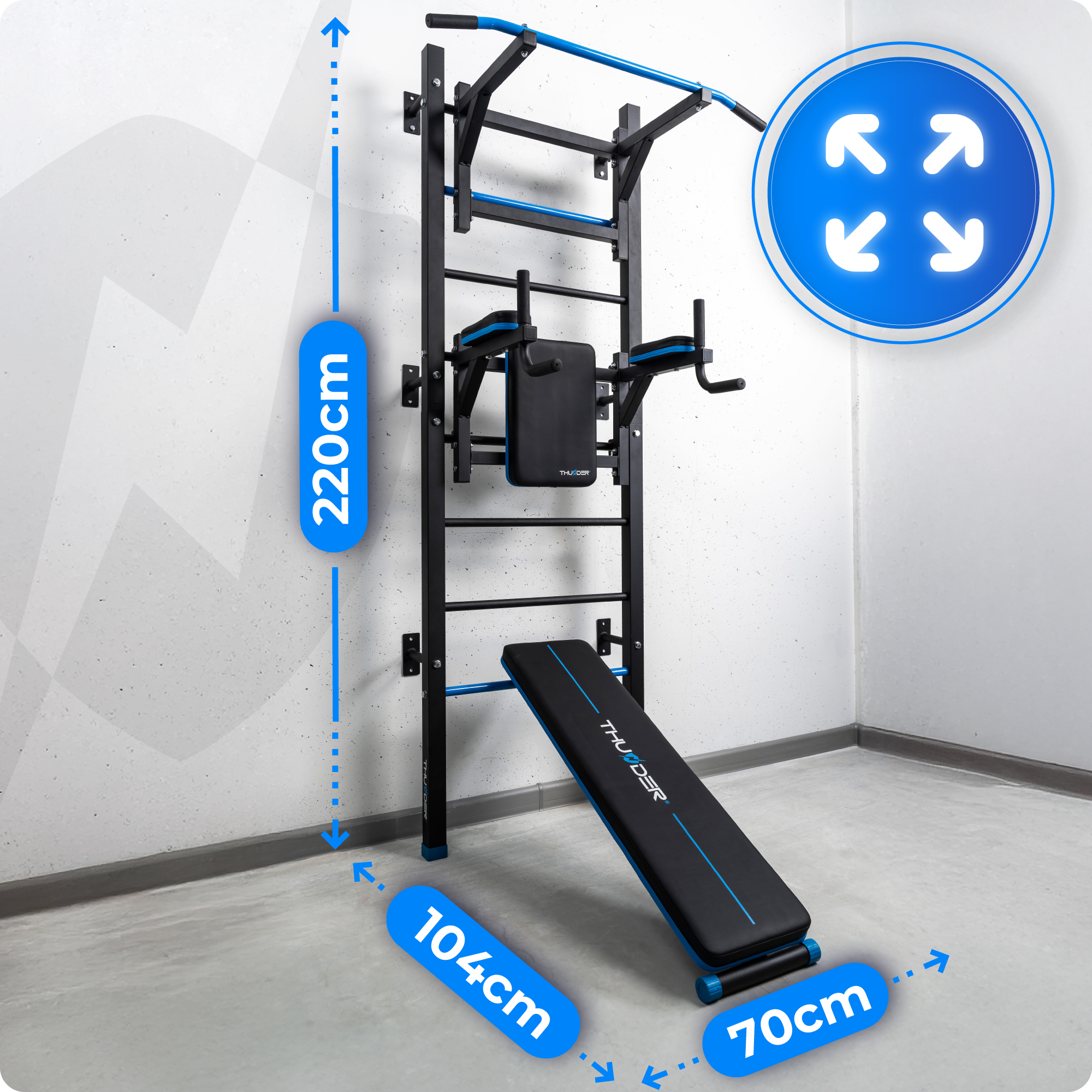Czarno-niebieska stacja treningowa stoi przy ścianie z pomiarami. Zawiera drążek do podciągania i ławkę.