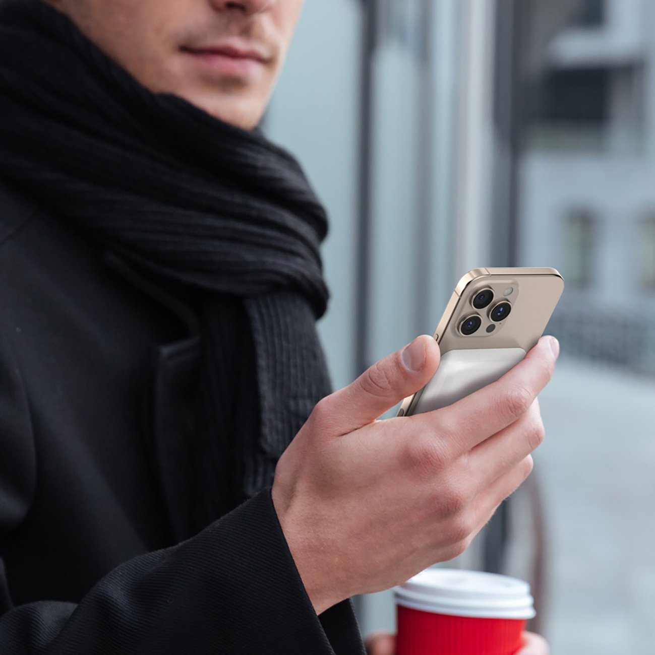 Mężczyzna trzyma złoty telefon z białą magnetyczną ładowarką w dłoni, z tłem miejskim.