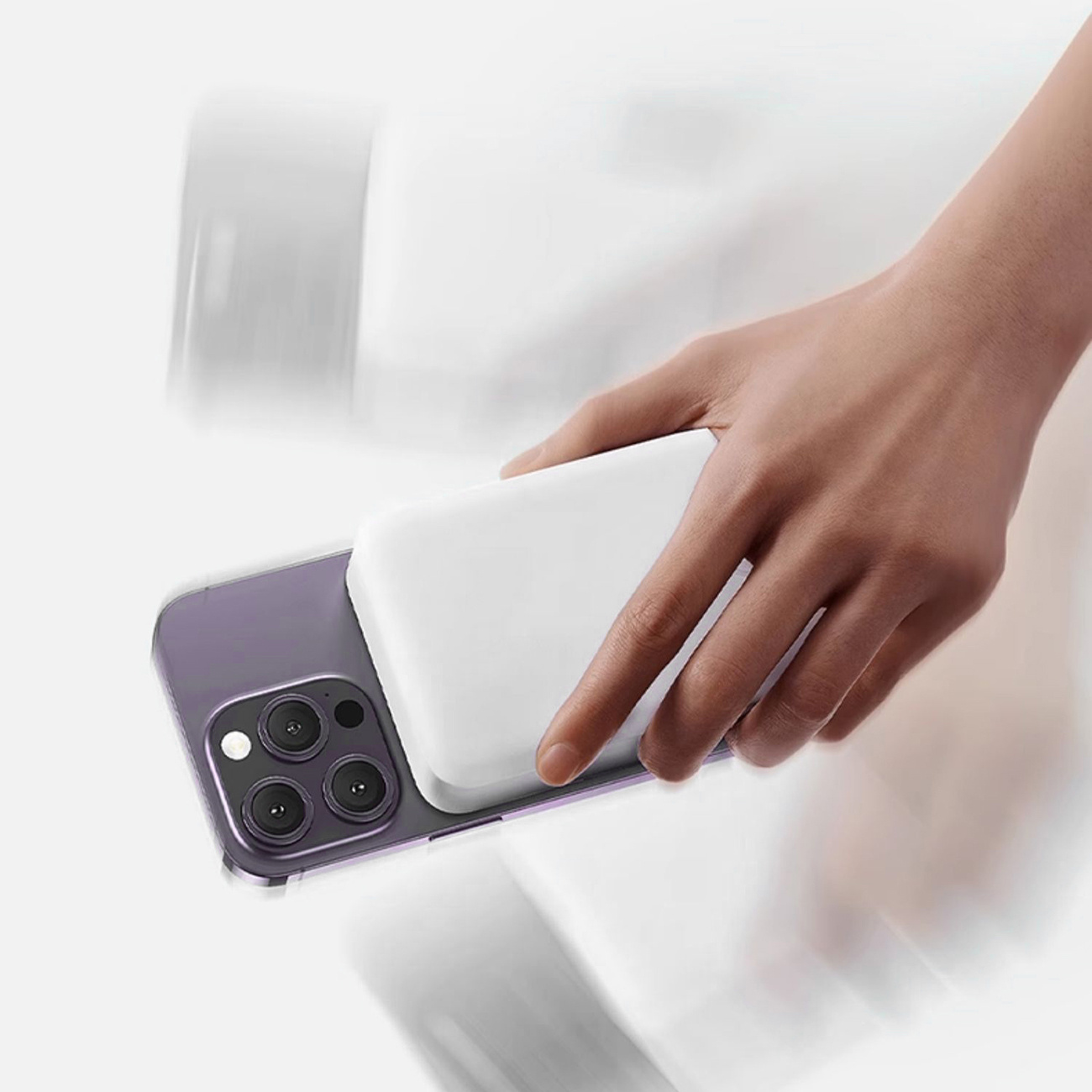 Dłoń umieszczająca białą podkładkę ładującą na fioletowym telefonie. Telefon leży na szarej powierzchni.