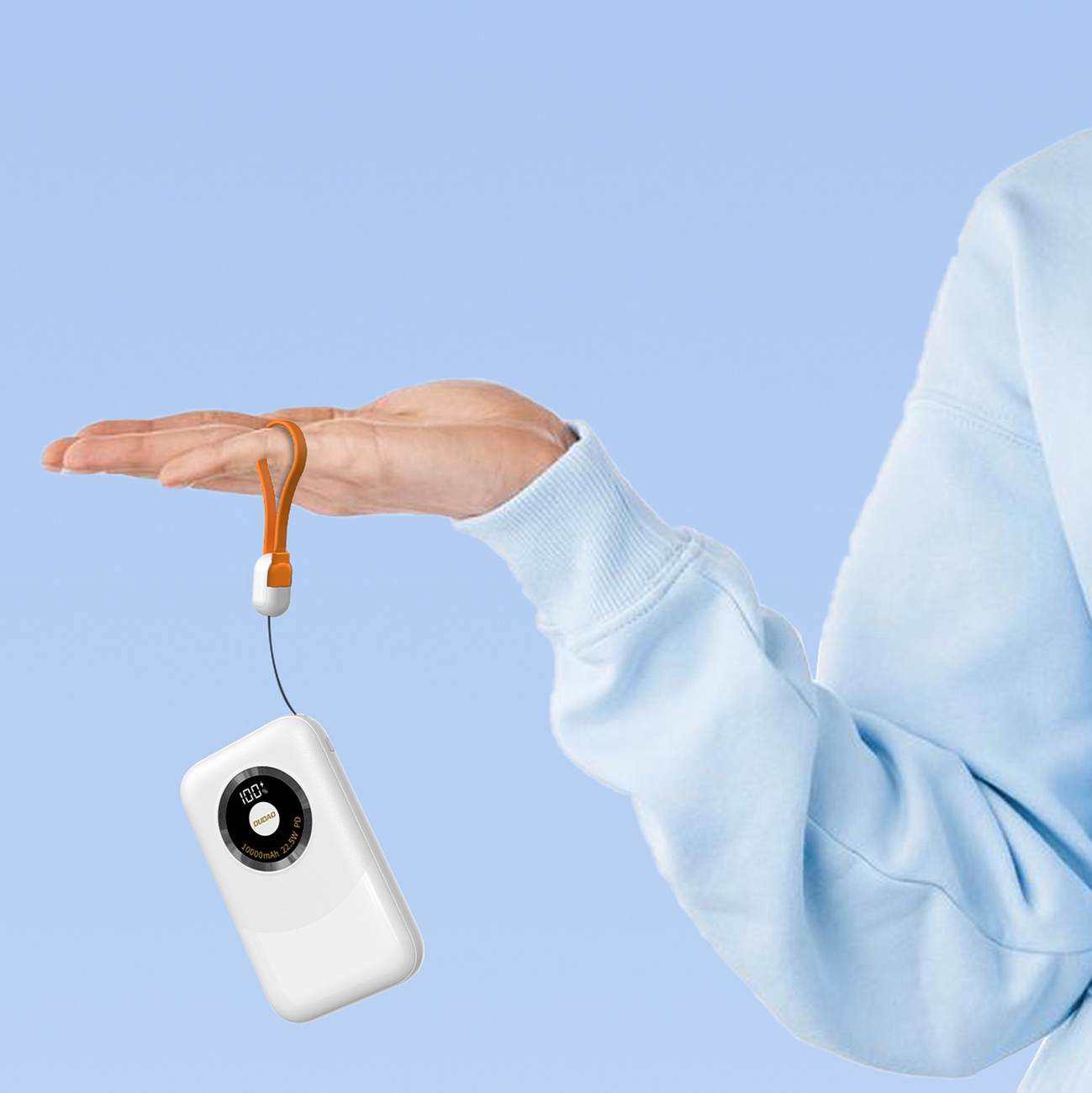 Dłoń trzymająca biały power bank z pomarańczowym paskiem na niebieskim tle.