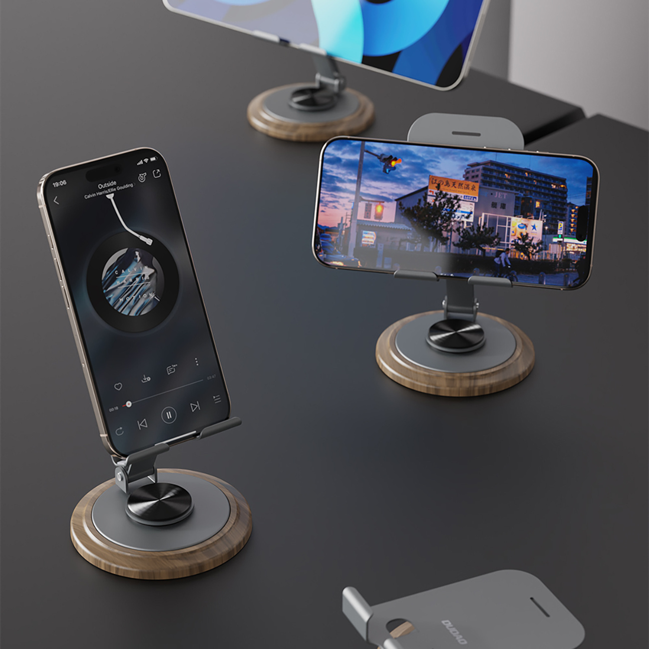 Kilka telefonów na stojakach, wyświetlających aplikacje muzyczne. Tło: ciemna powierzchnia i widok na miasto.