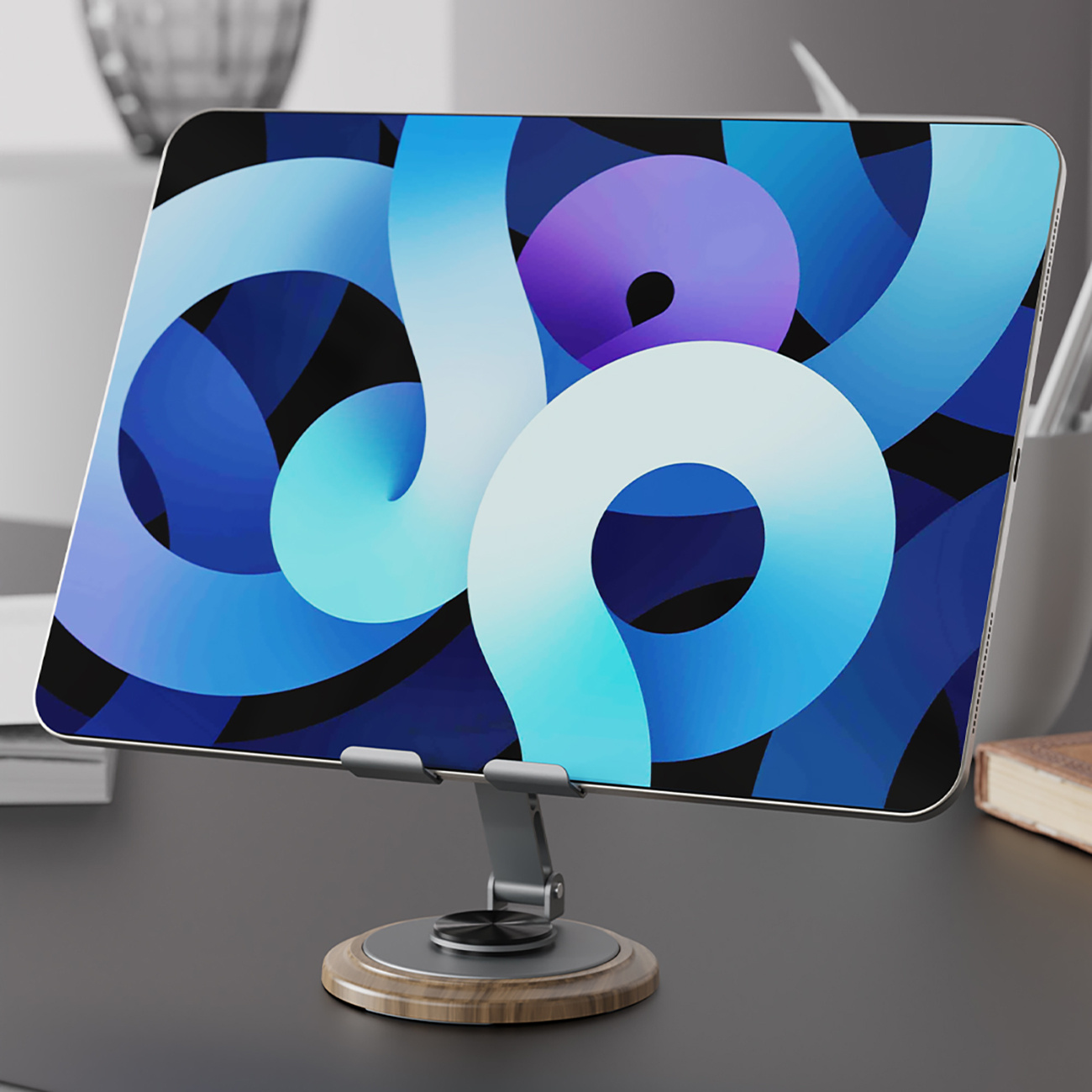 Tablet na stojaku, wyświetlający niebiesko-biały abstrakcyjny wzór. Stojak stoi na ciemnej powierzchni.