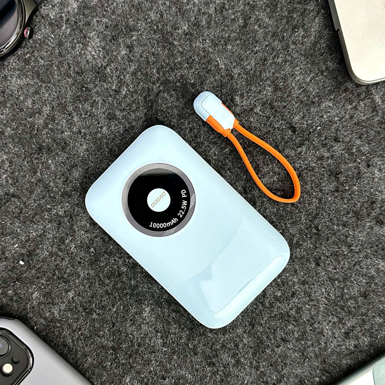 Jasnoniebieska ładowarka z czarnym okręgiem. Dołączony jest czarno-pomarańczowy pasek.