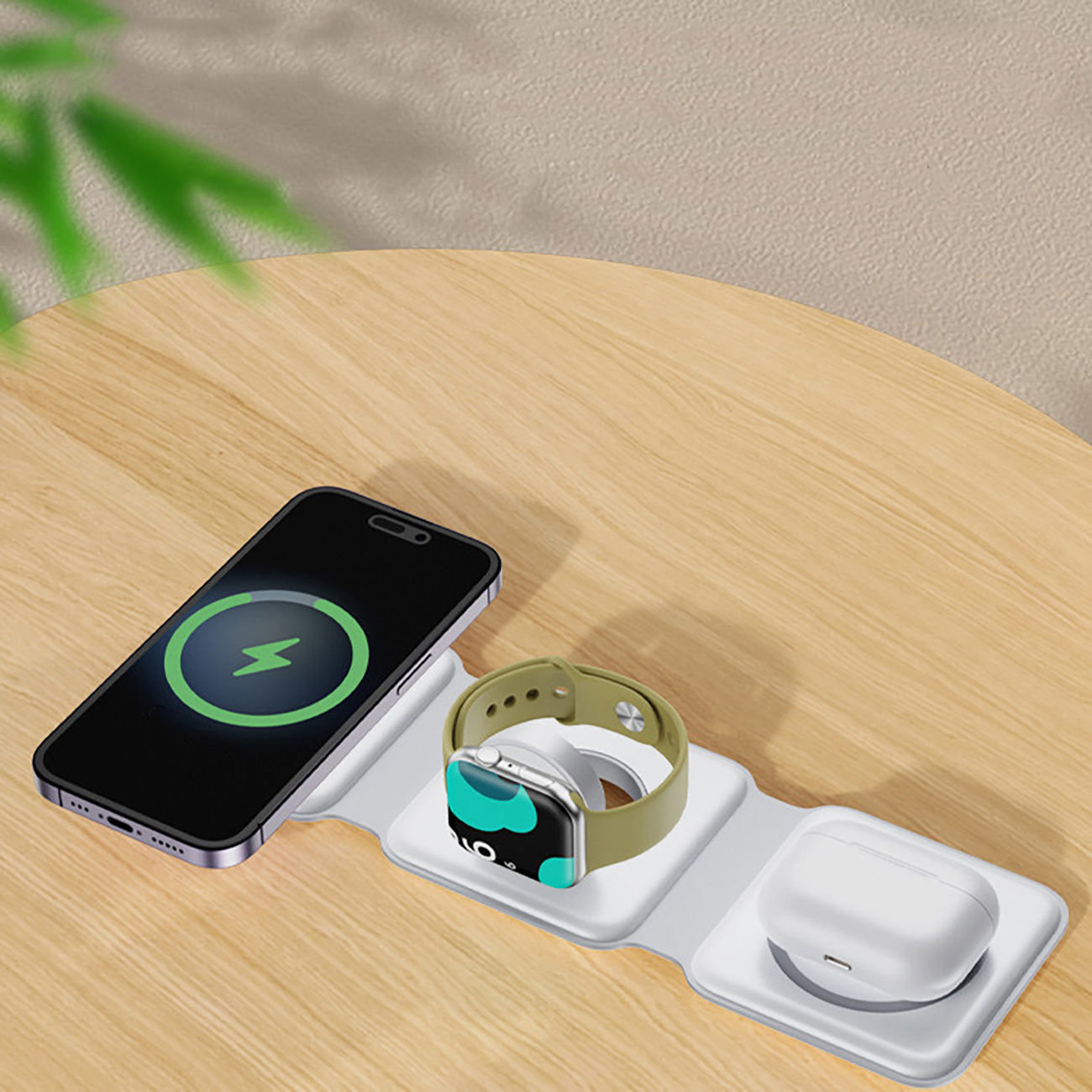 Ładowarka bezprzewodowa z telefonem, zegarkiem i etui na słuchawki. Telefon się ładuje. Drewniany stół, białe tło.