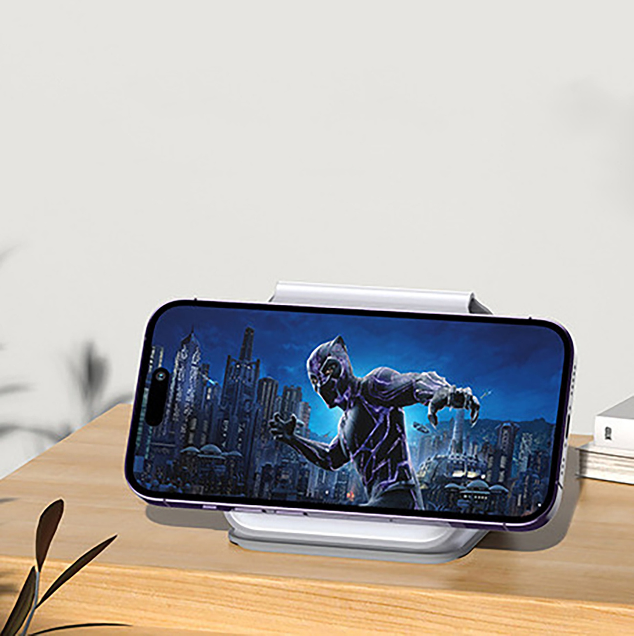 Telefon na stojaku z Czarną Panterą. Drewniany stół, biała ściana w tle.