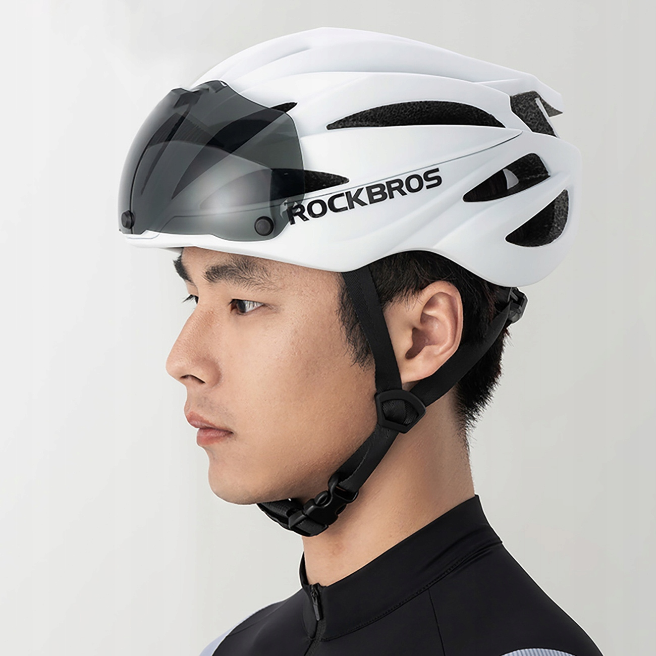 Osoba ma na sobie biały kask rowerowy z ciemną osłoną. Widoczna jest marka ROCKBROS.