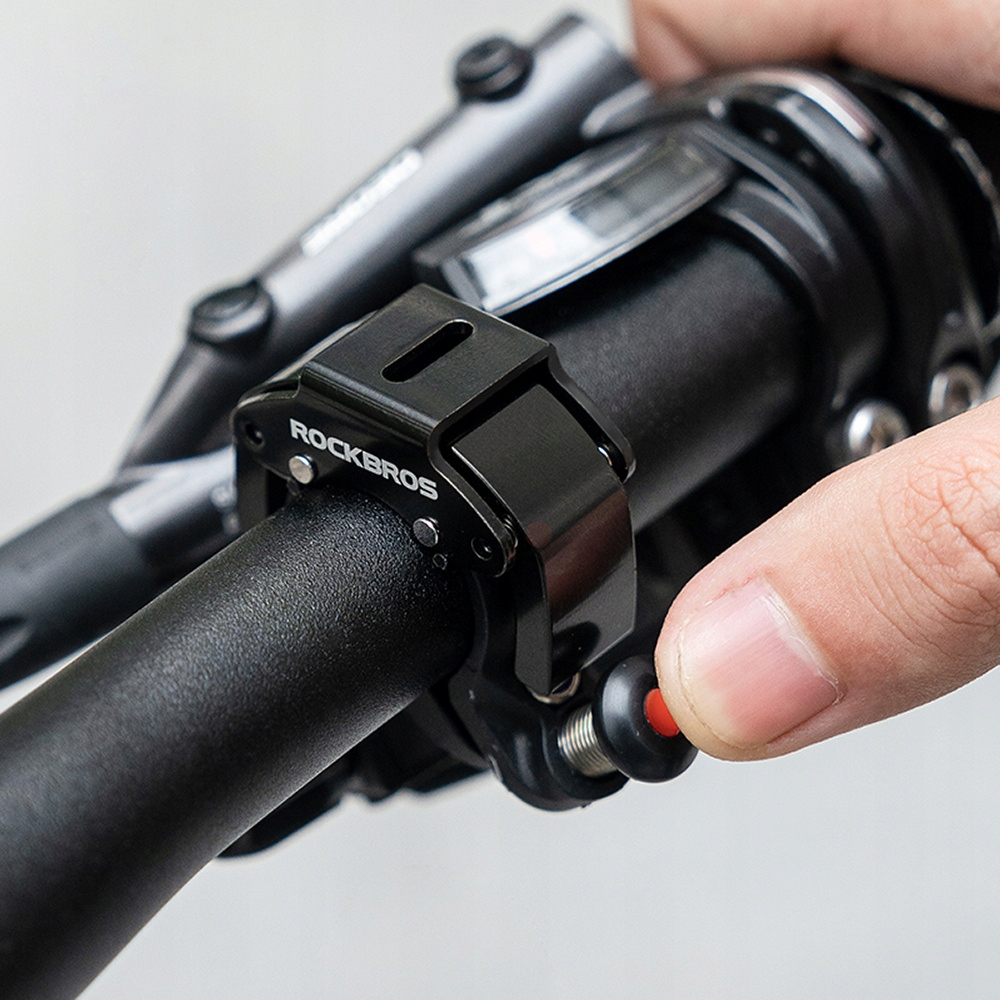 Ręka naciska czerwony przycisk na czarnym uchwycie do lampki rowerowej ROCKBROS przymocowanym do kierownicy.