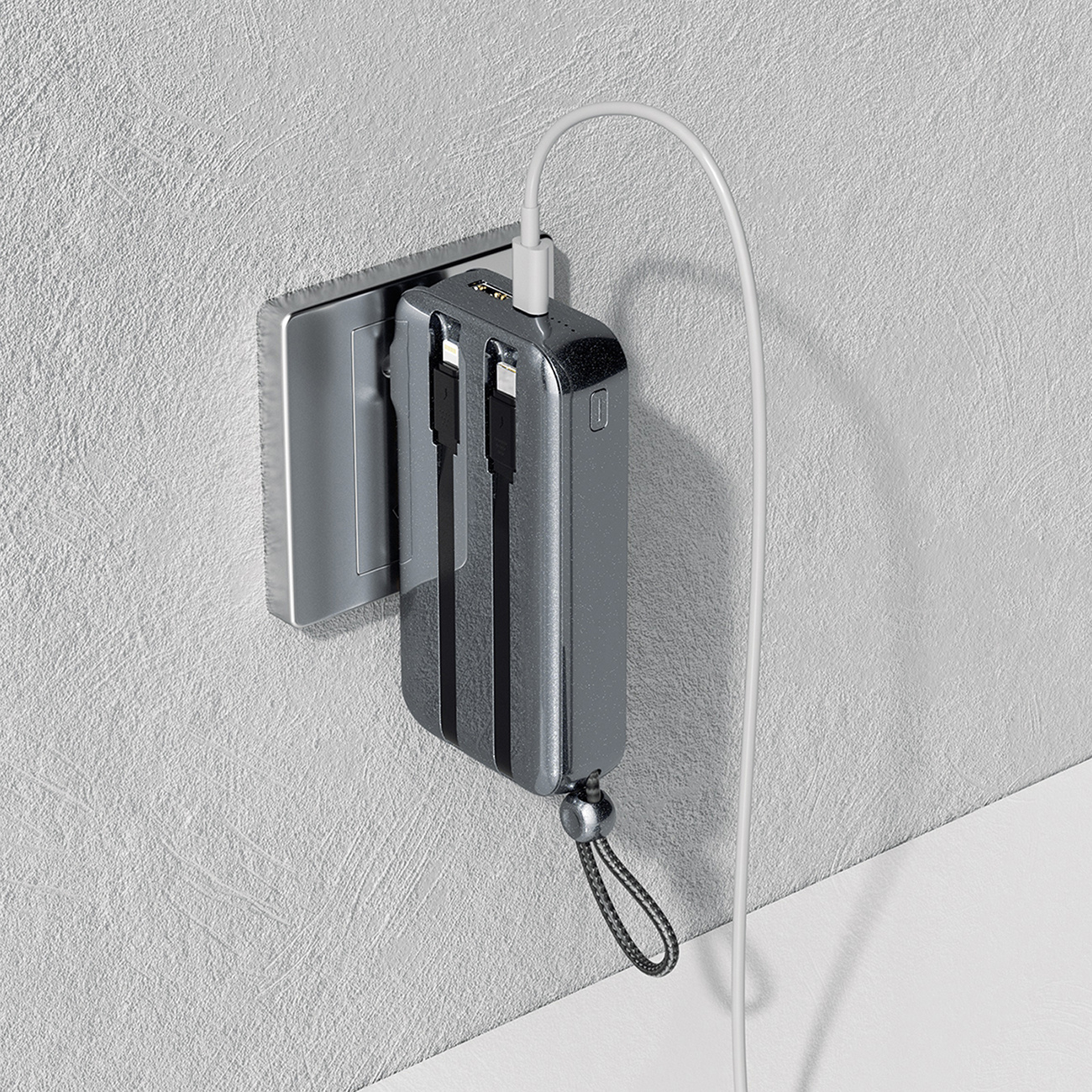 Power bank podłączony do gniazdka ściennego. Biały kabel rozciąga się w prawo. Szare tło ściany.