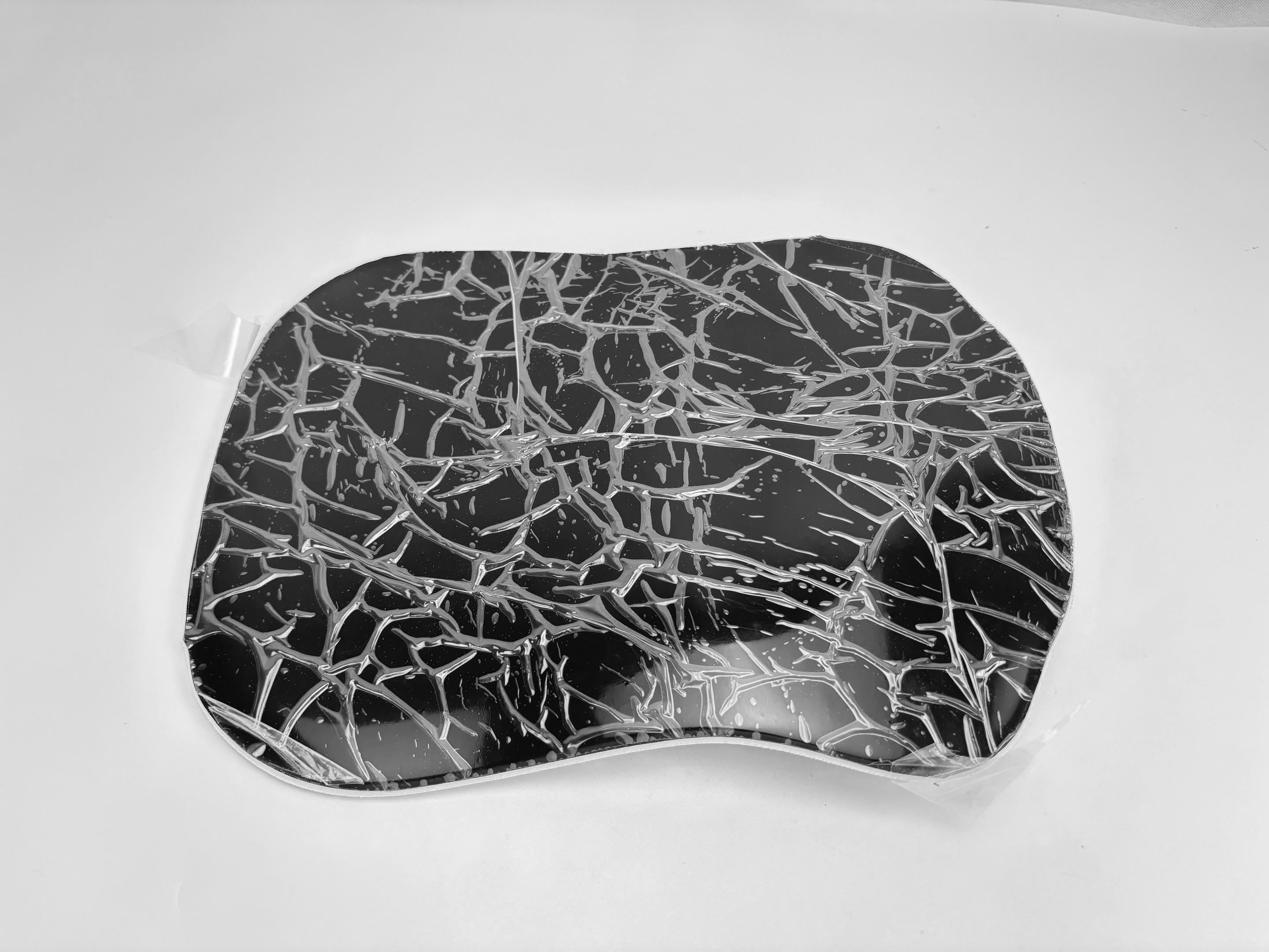 Ein schwarzes und silbernes Mauspad mit Rissglas-Effekt. Das Pad liegt auf einer weißen Oberfläche.