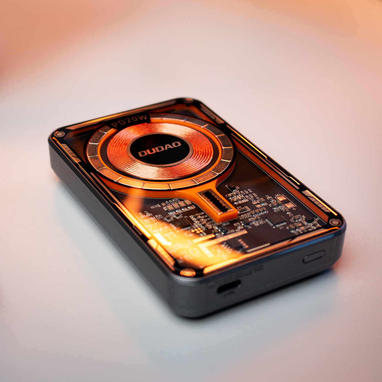 Czarno-pomarańczowy power bank z widoczną cewką ładowania bezprzewodowego.