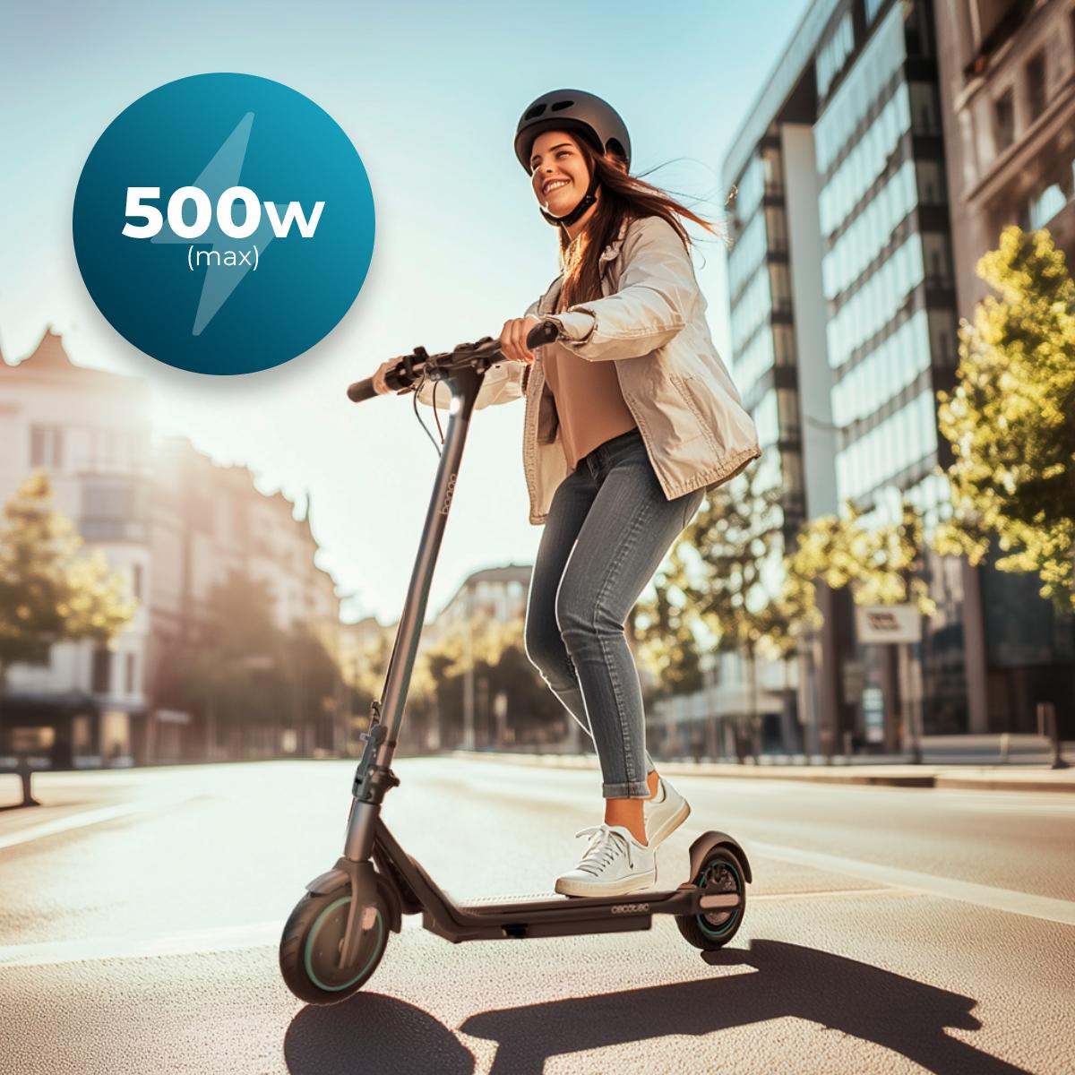 Una donna con un casco guida uno scooter. Un grafico mostra 500W di potenza. Edifici e cielo blu sullo sfondo.