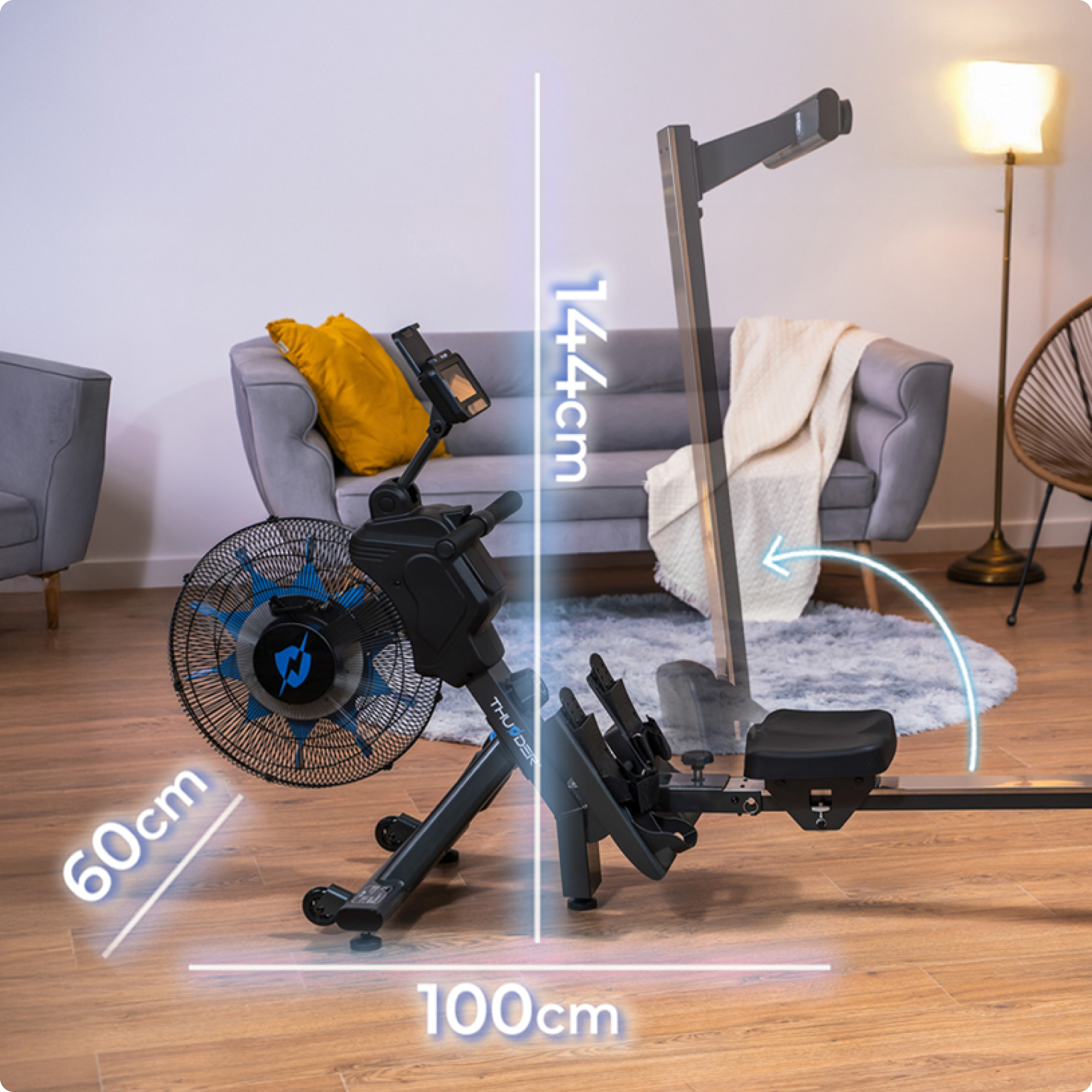 Wioślarz ze wyświetlonymi wymiarami. Widoczny wentylator i ekran. Szara sofa w tle.