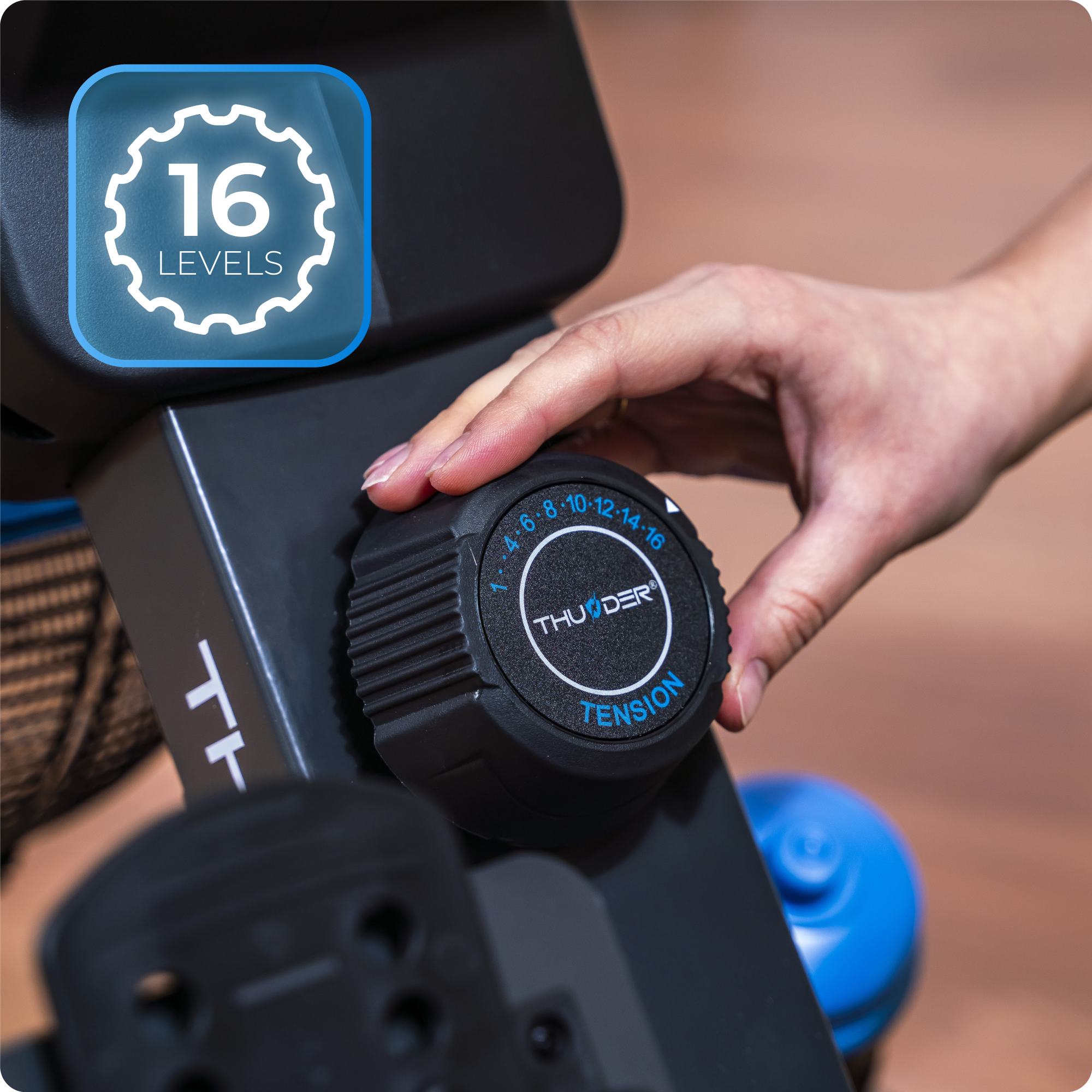 Ręka regulująca pokrętło oporu na wioślarzu. Tekst brzmi '16 Poziomów' i 'Napięcie'.