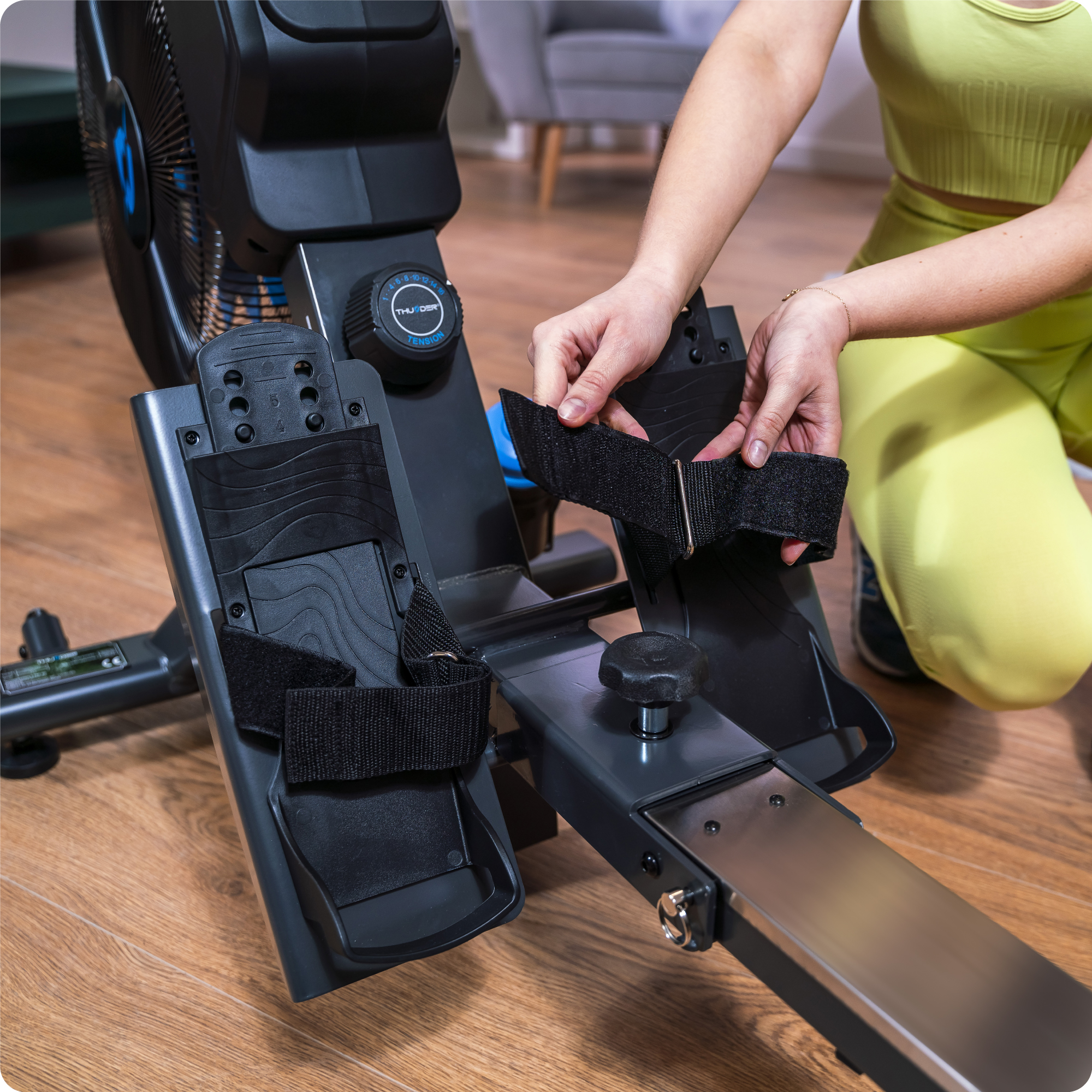 Ręce mocujące paski na stopy do wioślarza. Maszyna jest czarno-srebrna.