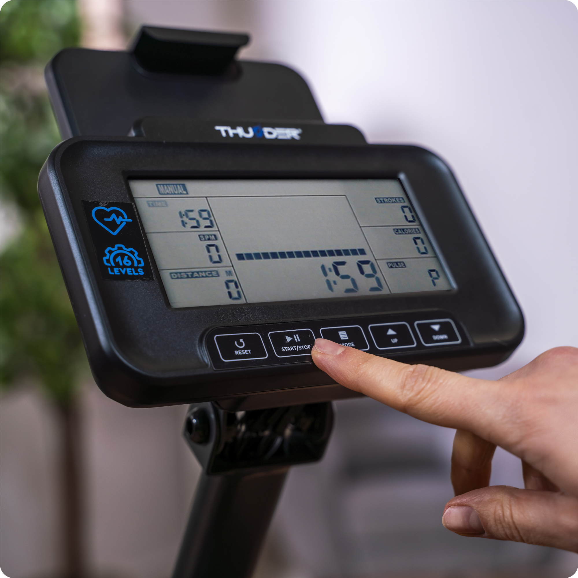 Zbliżenie ekranu wioślarza wyświetlającego czas, prędkość i kalorie. Palec naciska przycisk.