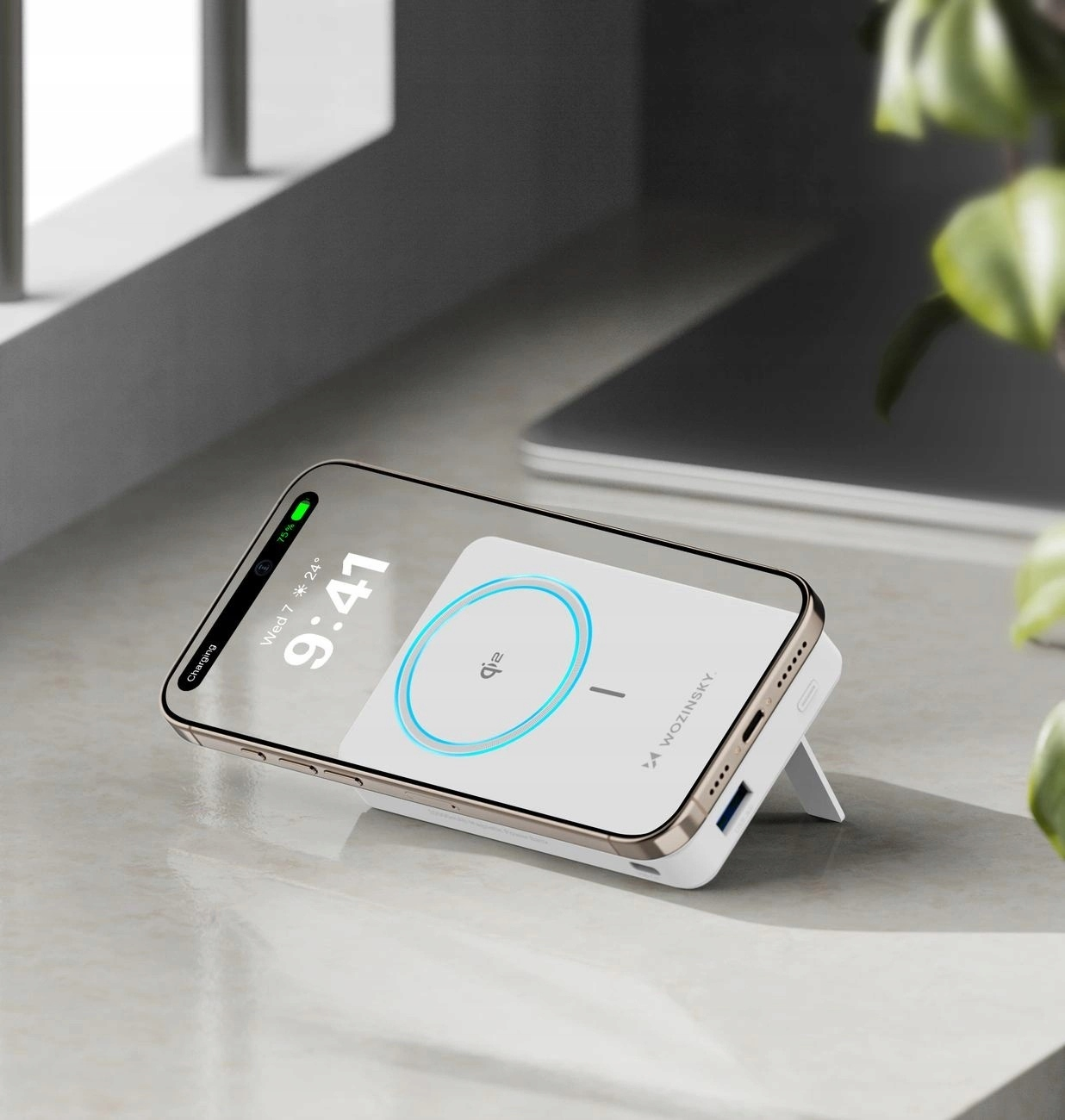 Telefon ładujący się na białej ładowarce bezprzewodowej. Ładowarka jest na biurku z laptopem.