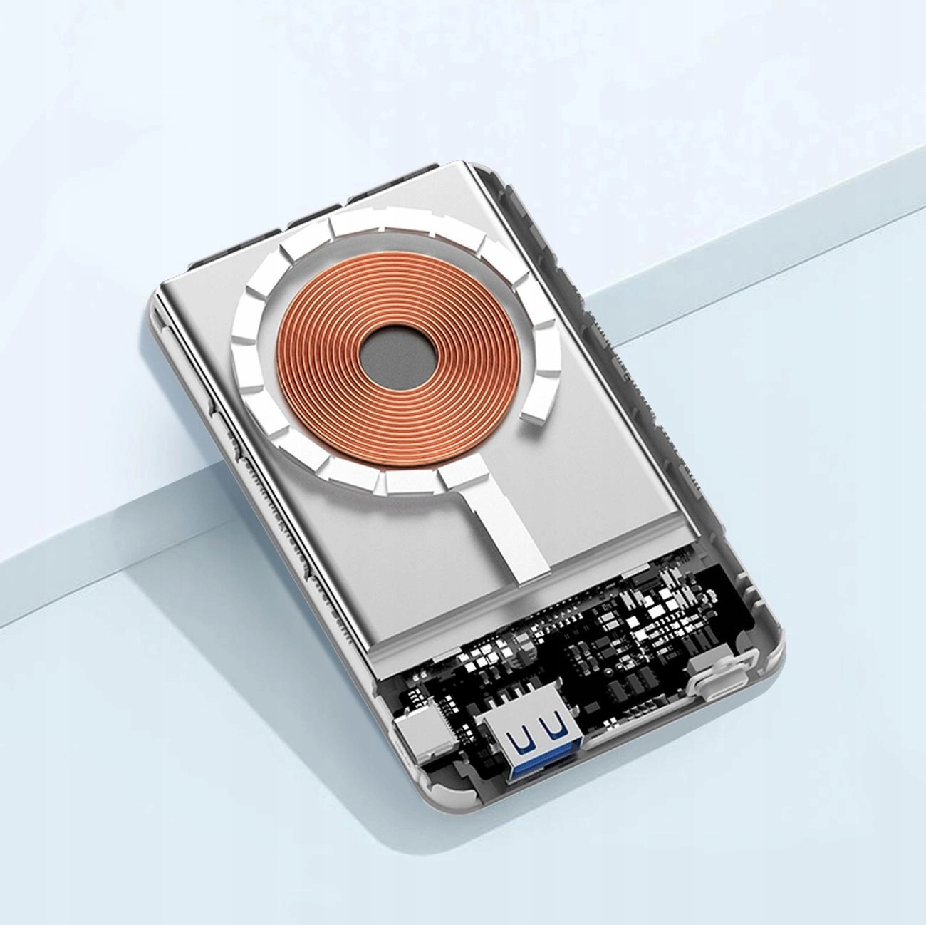 Power bank, otwarty, pokazujący wewnętrzne elementy. Ma brązową cewkę i dwa porty USB.