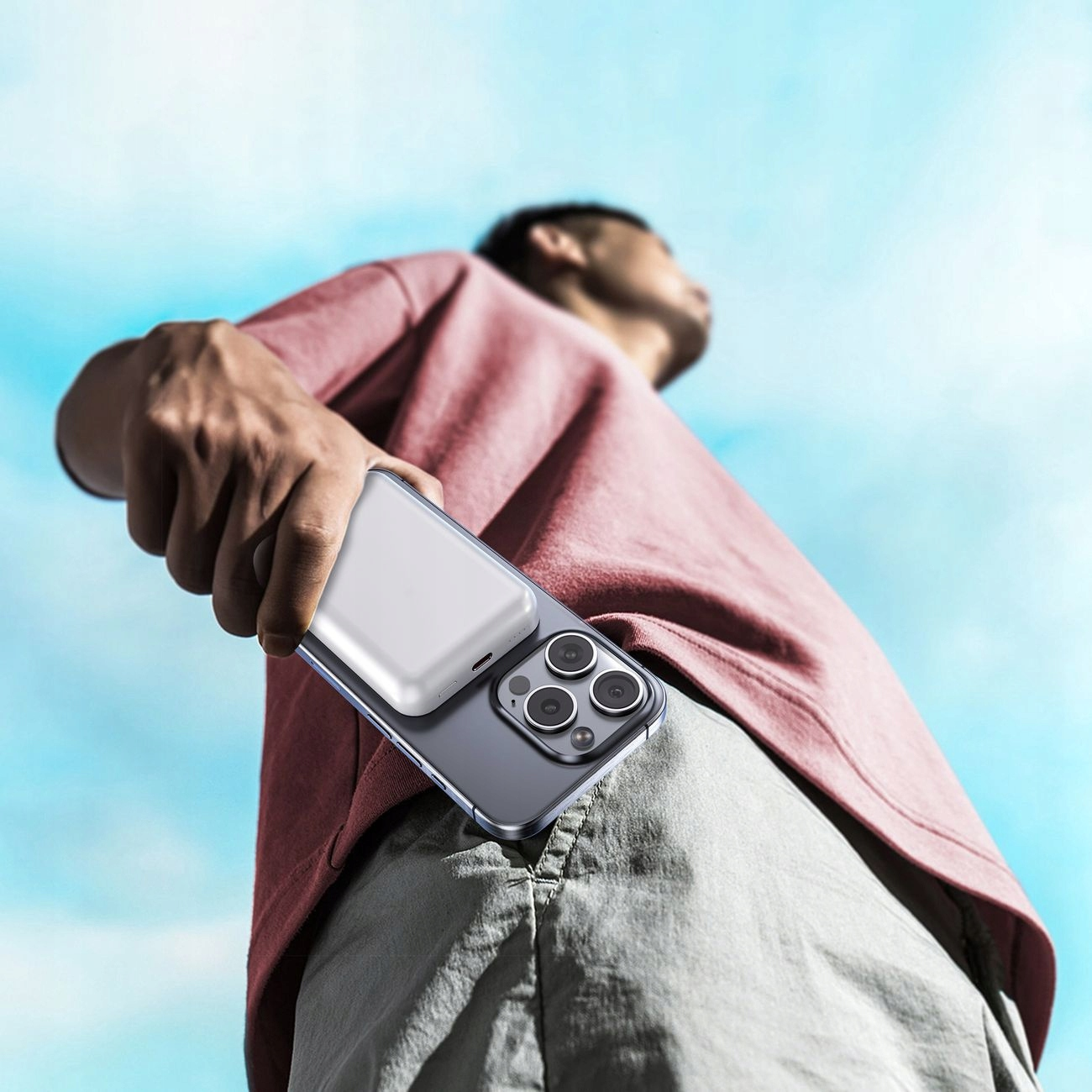 Osoba trzymająca fioletowy telefon z dołączonym srebrnym power bankiem. Błękitne niebo.