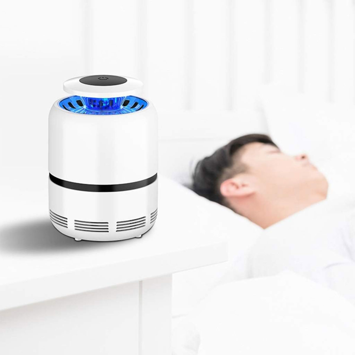 Trampa para mosquitos cilíndrica blanca con luz azul en una mesita de noche blanca junto a una persona durmiendo.