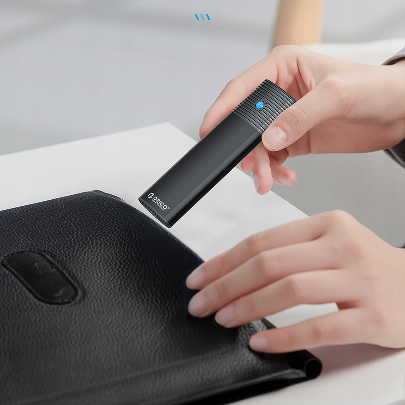 Osoba trzymająca czarny zewnętrzny dysk twardy nad czarnym portfelem. Dysk ma niebieskie światło.