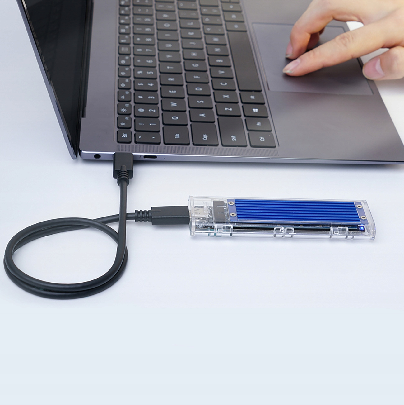 Laptop z przezroczystym zewnętrznym dyskiem twardym podłączonym kablem USB-C. Ręka używa touchpada.