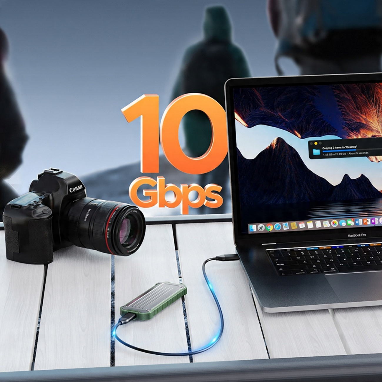 Aparat i laptop stoją na stole. Tekst '10 Gbps' znajduje się na środku. Postać idzie w tle.