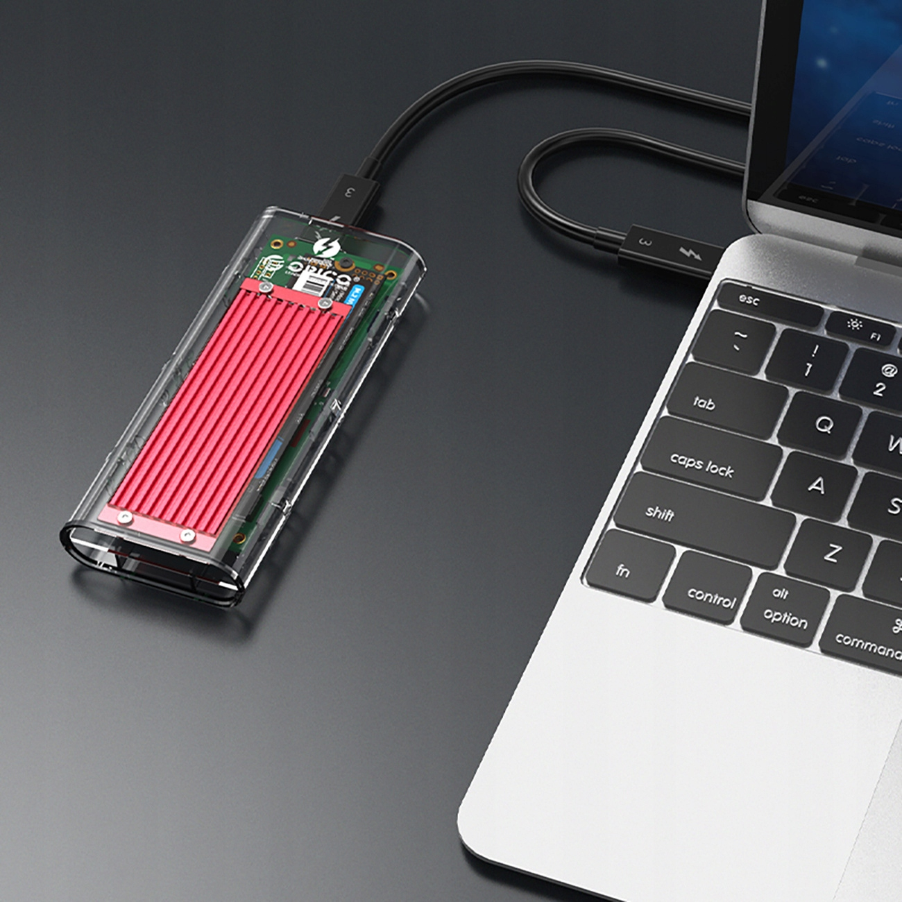 Laptop z zewnętrznym dyskiem twardym podłączonym kablem USB-C. Czerwony metalowy element w środku.