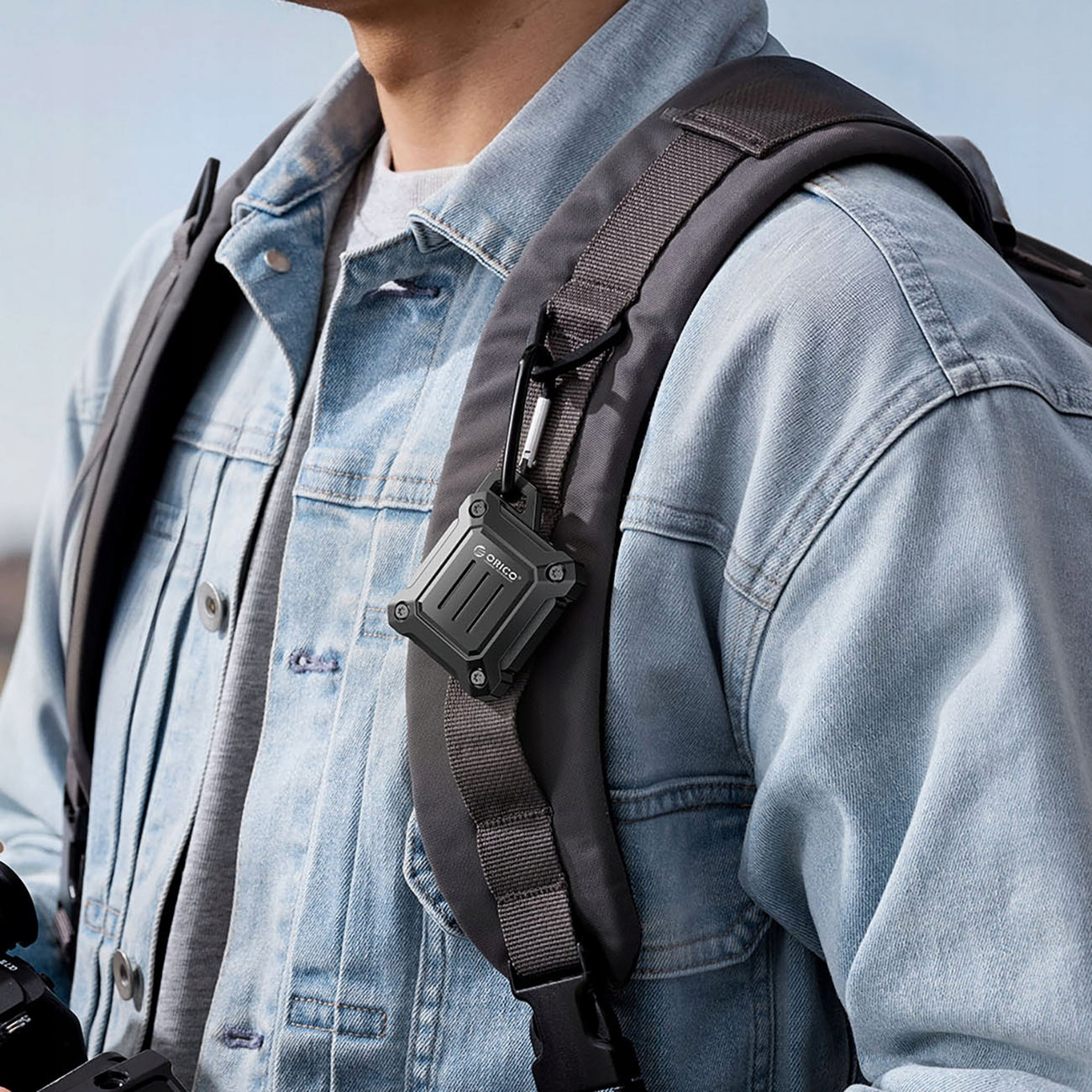 Osoba w dżinsowej kurtce z czarnym urządzeniem przypiętym do paska plecaka.