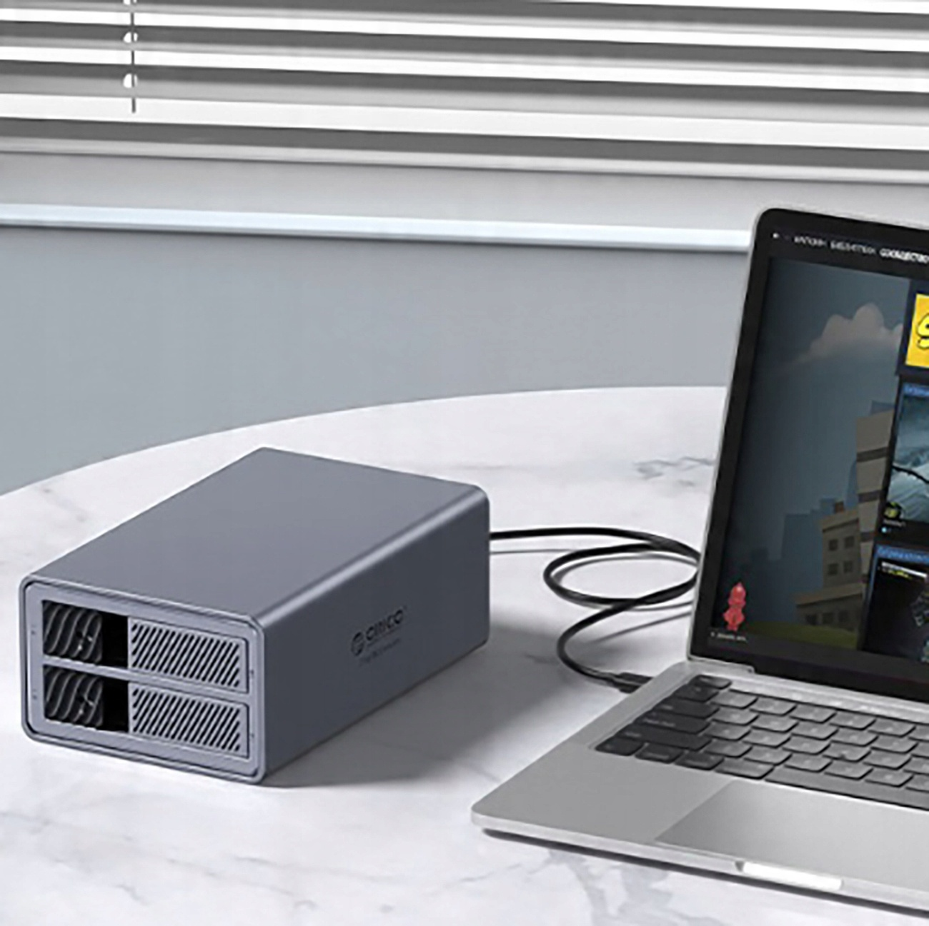 Obudowa zewnętrznego dysku twardego podłączona do laptopa. Obudowa jest szara, laptop otwarty.