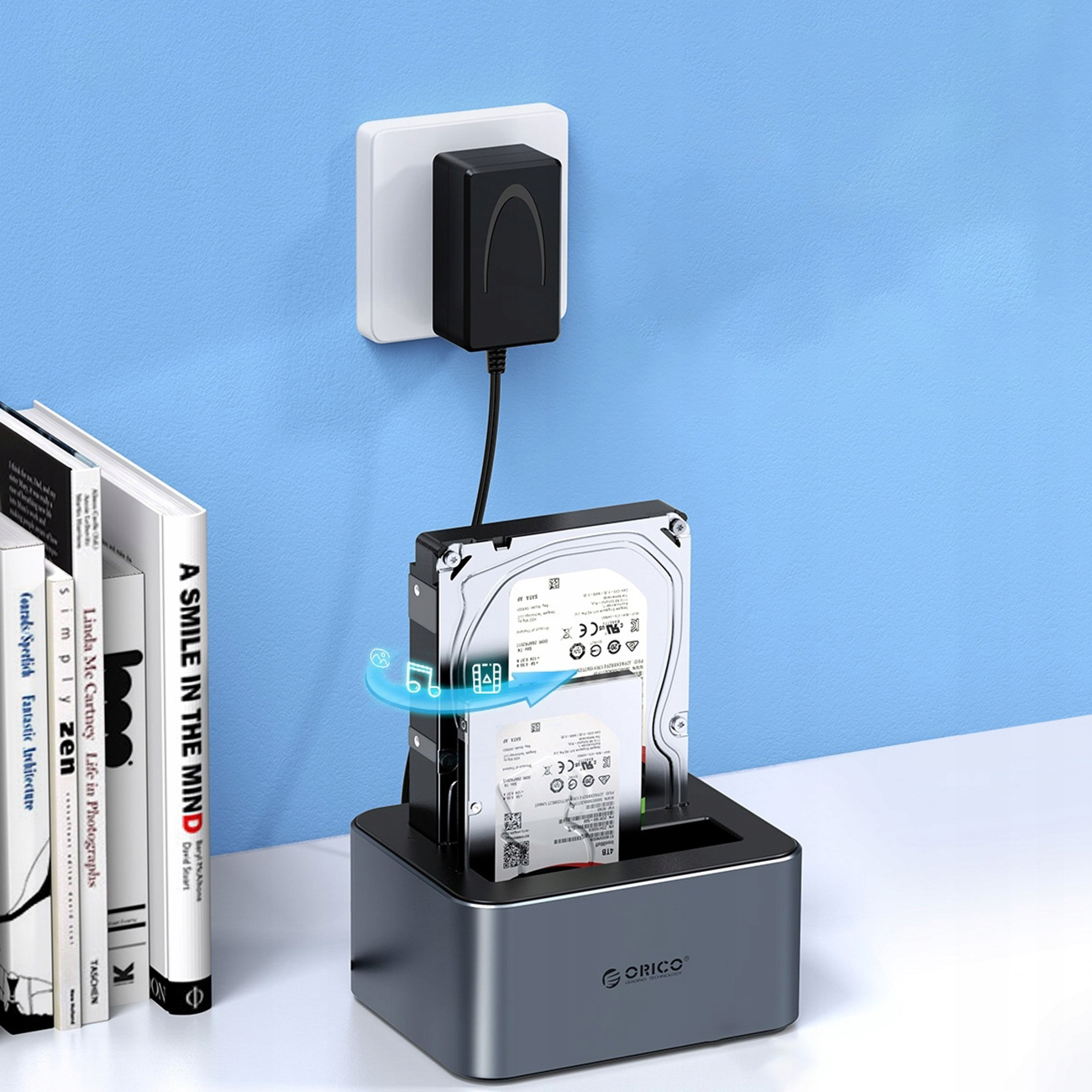 Dysk twardy w stacji dokującej obok książek i zasilacza.