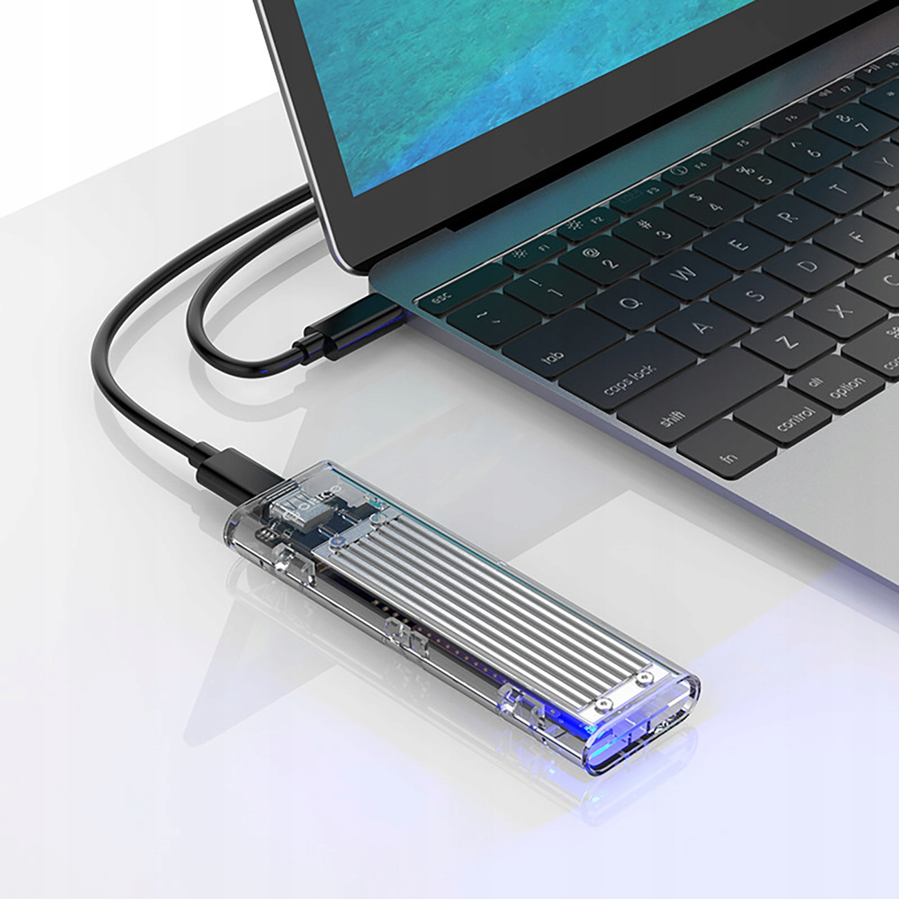 Przezroczysta obudowa SSD podłączona do laptopa za pomocą kabla USB. Widoczne niebieskie światło.