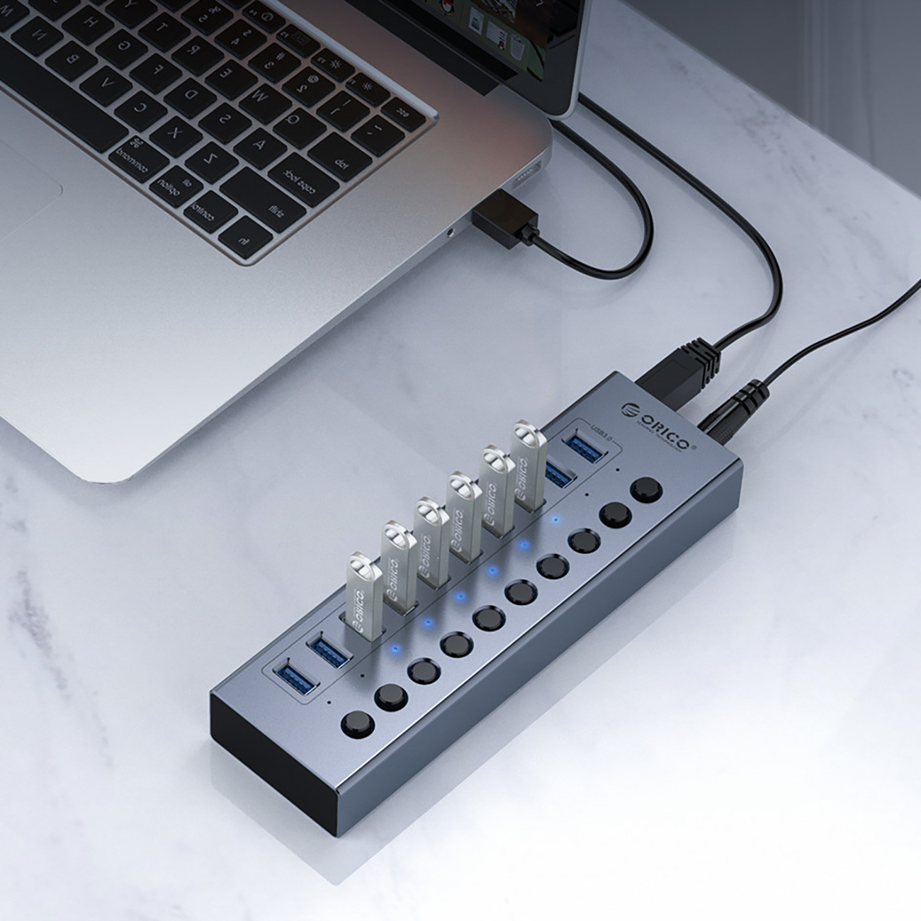 Hub USB podłączony do laptopa. Marka Orico. Tło jest białe.