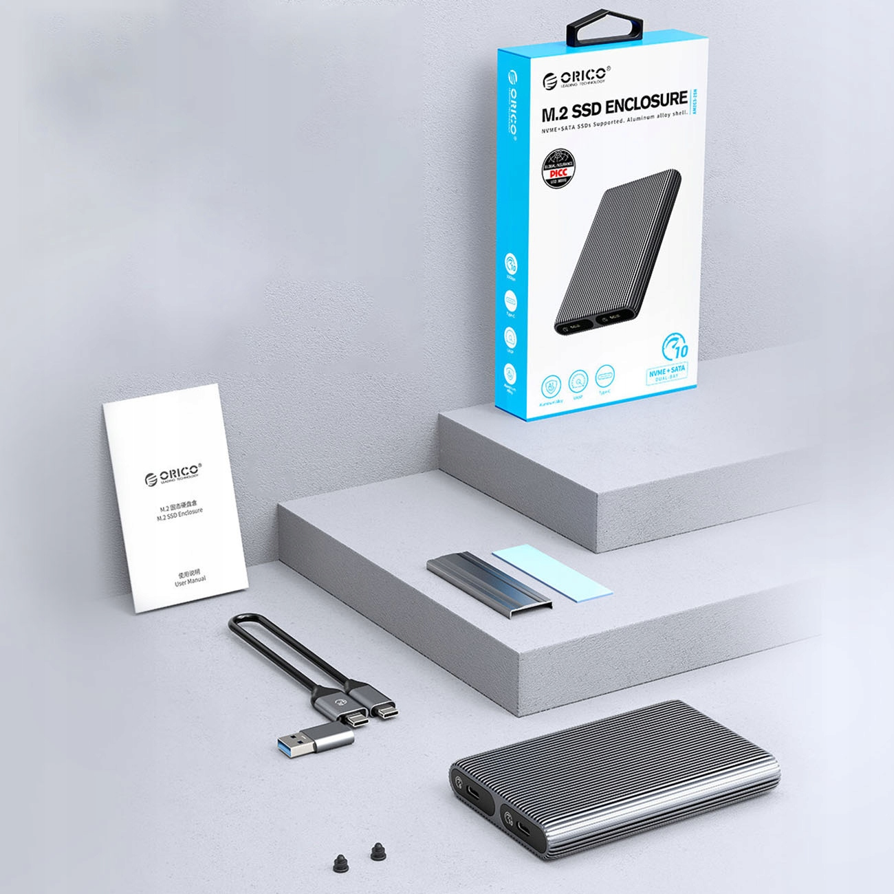Un kit alloggiamento SSD con una scatola, un manuale, un cavo e un'unità. Tutto su una superficie bianca.