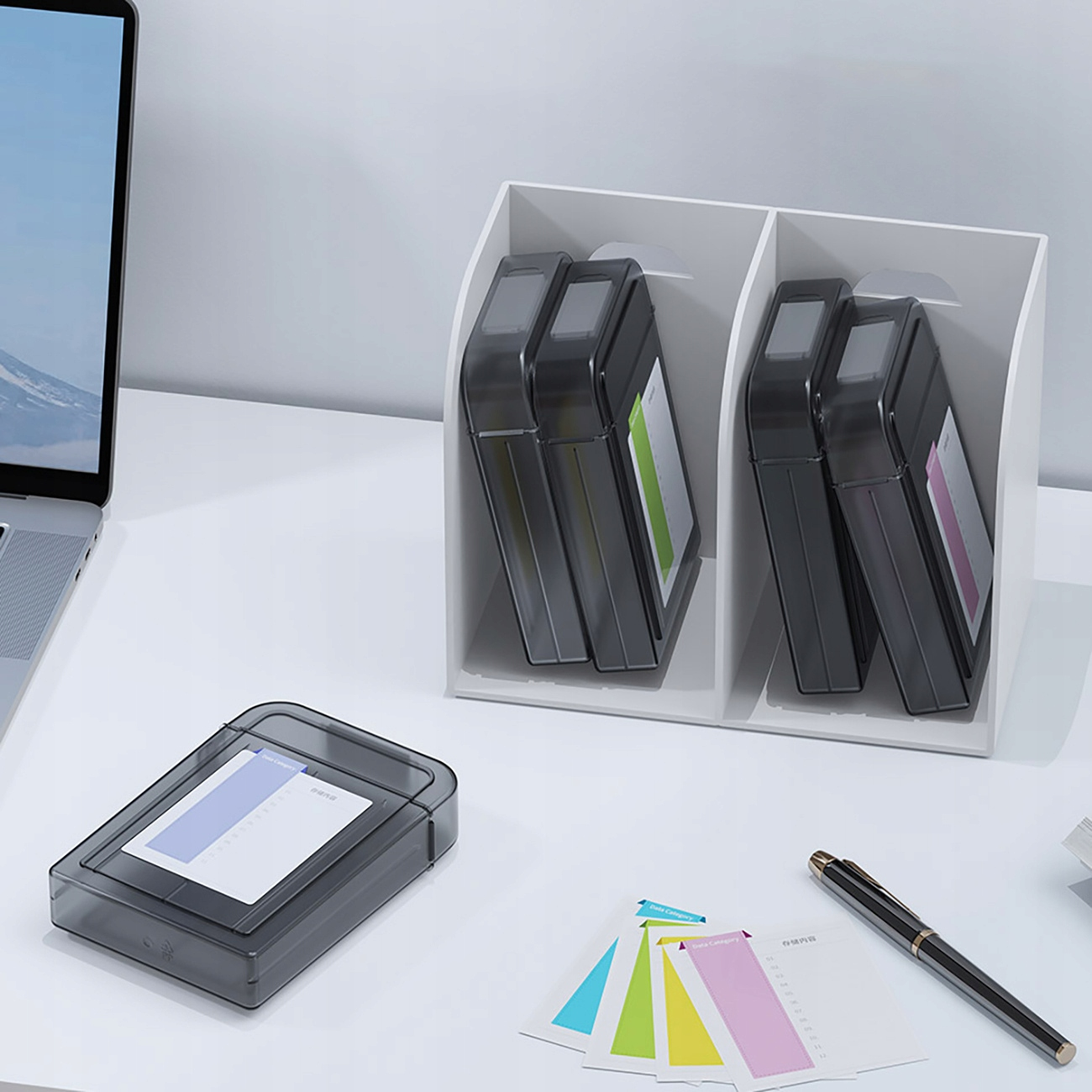 Biały organizer biurkowy z czterema etui na dyski twarde. Widoczny jest długopis i karteczki samoprzylepne. Białe tło.