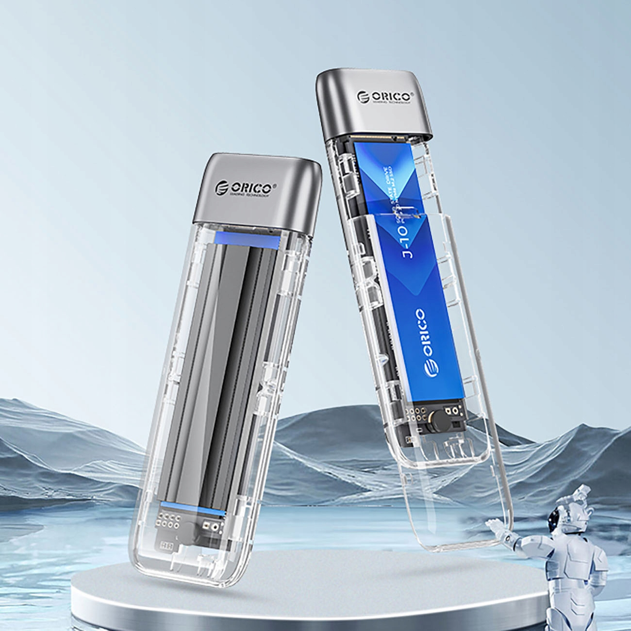 Dwie przezroczyste obudowy z czarnym wnętrzem, na srebrnej podstawce z robotem w tle.