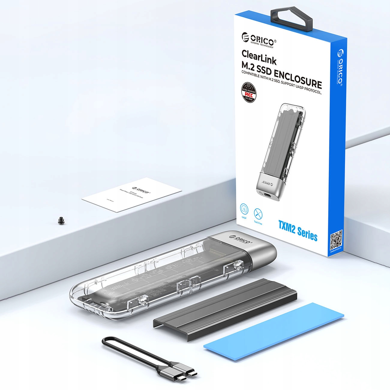Pudełko z obudową SSD i akcesoriami. Widoczna nazwa marki „ORICO”. Produkt to seria TXM2.