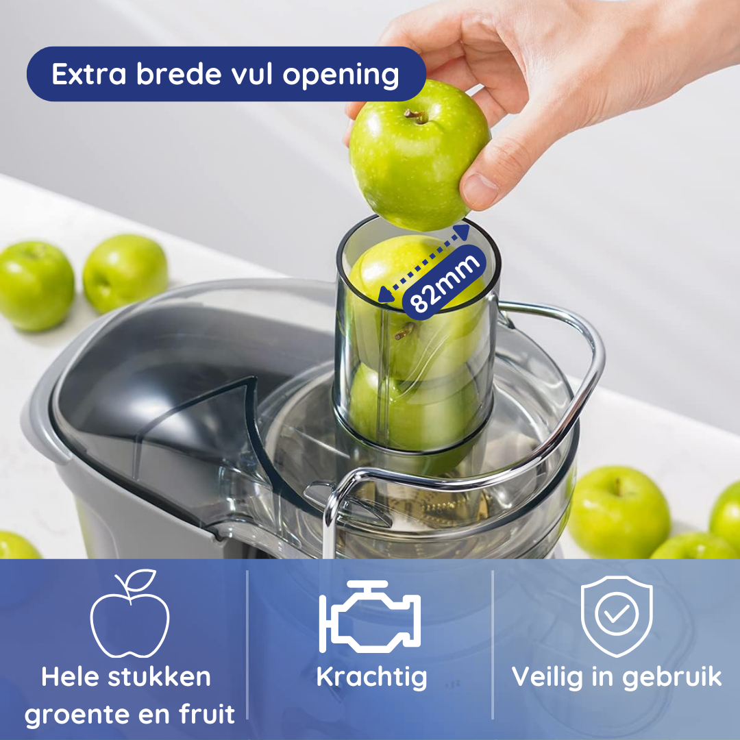 A juicer with a hand placing an apple in the opening. Green apples are on the white surface.