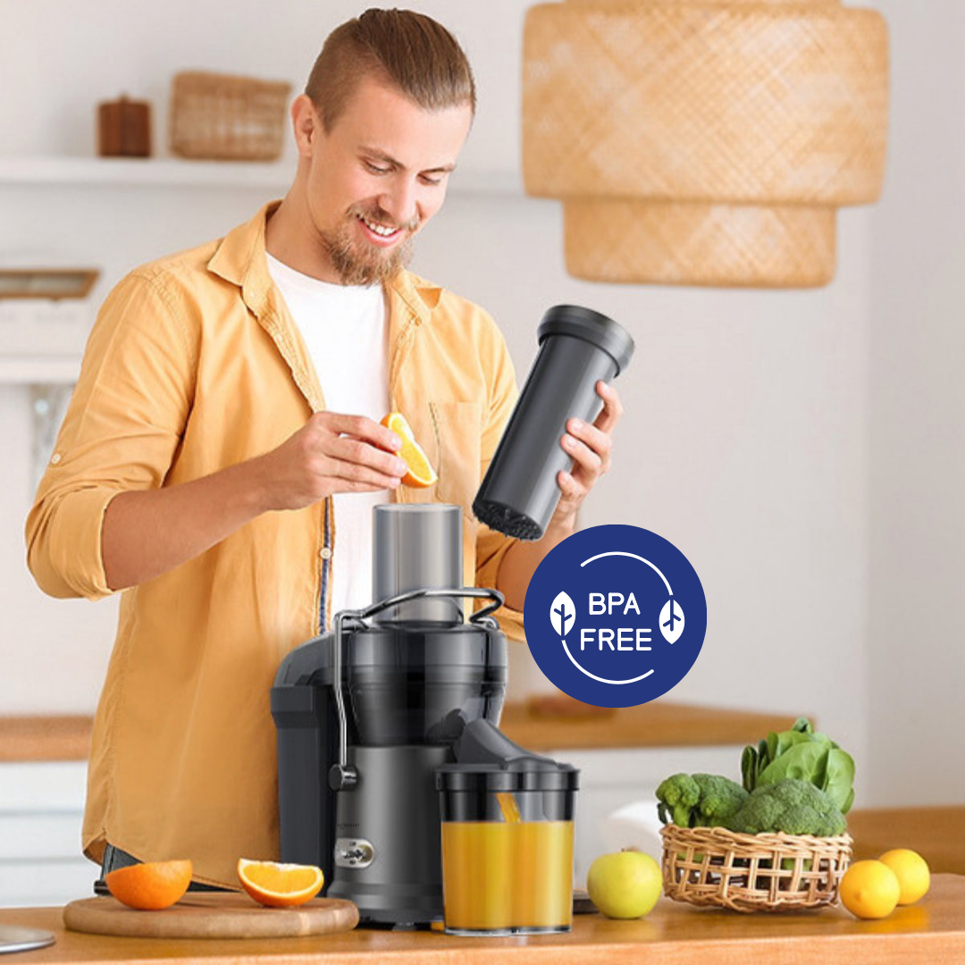 A man near a juicer holding an orange slice, with fruits and vegetables.