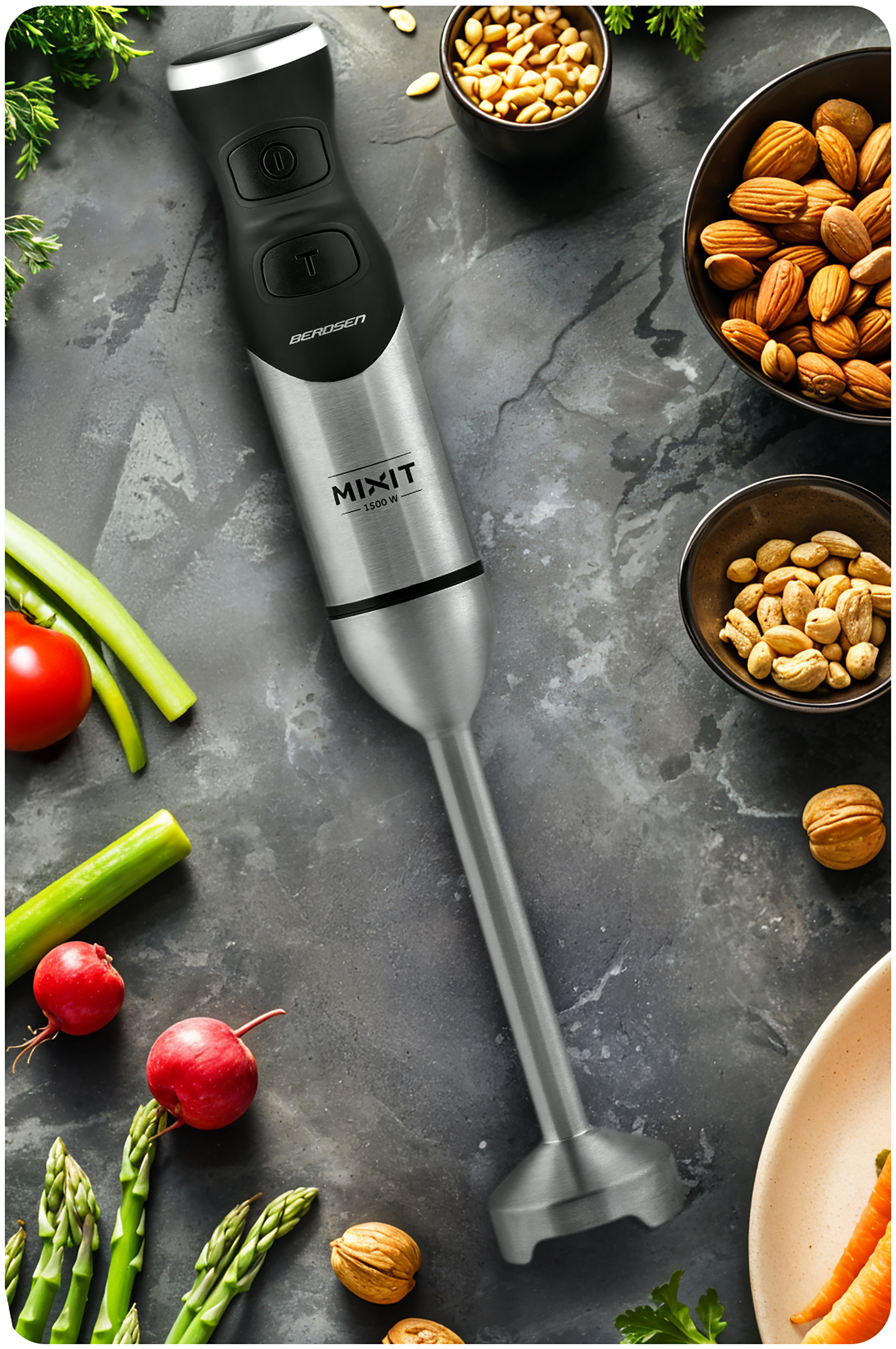 Srebrny blender ręczny na ciemnym tle, otoczony warzywami i orzechami.