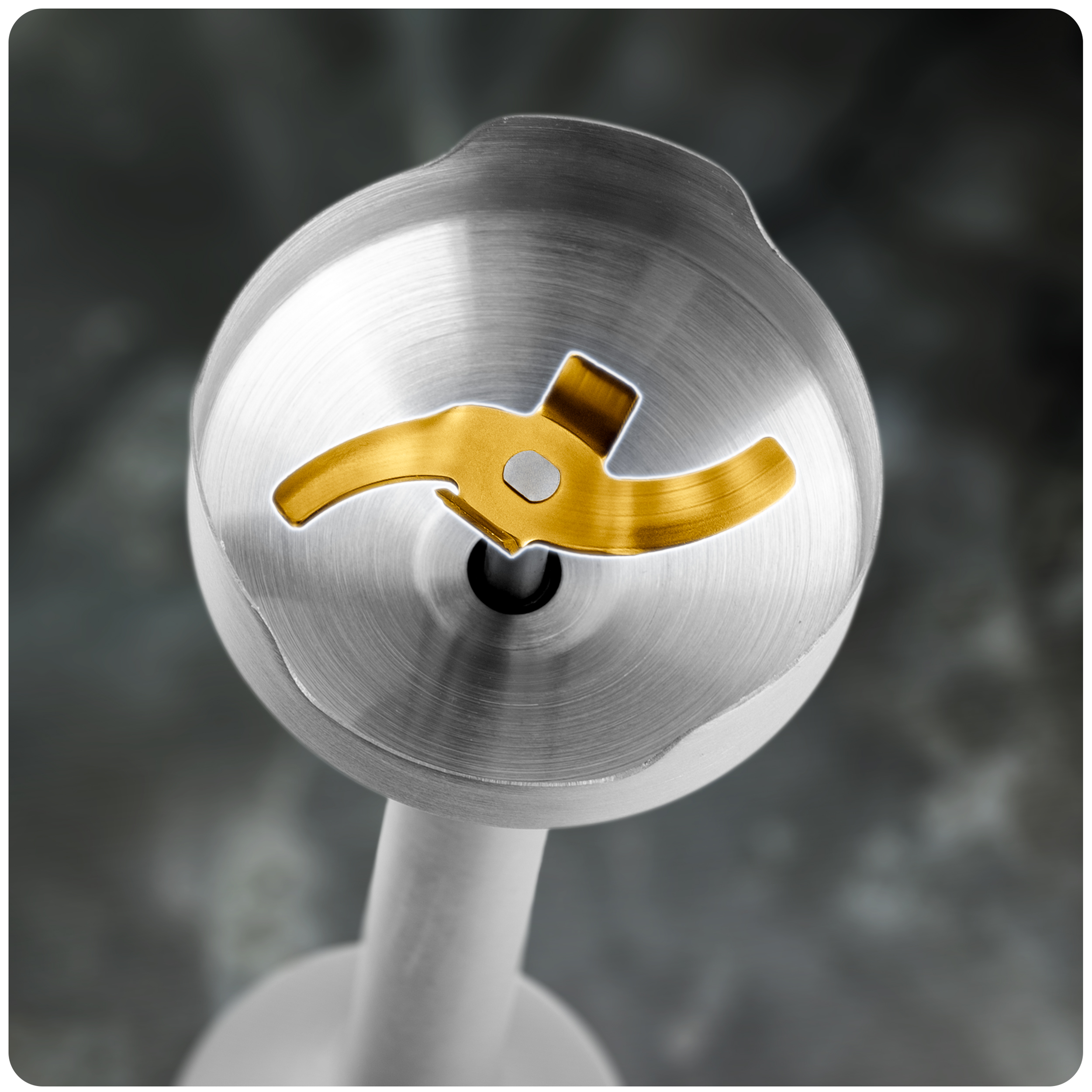 Zbliżenie głowicy blendera ręcznego ze złotym ostrzem, otoczonej metalową powierzchnią.