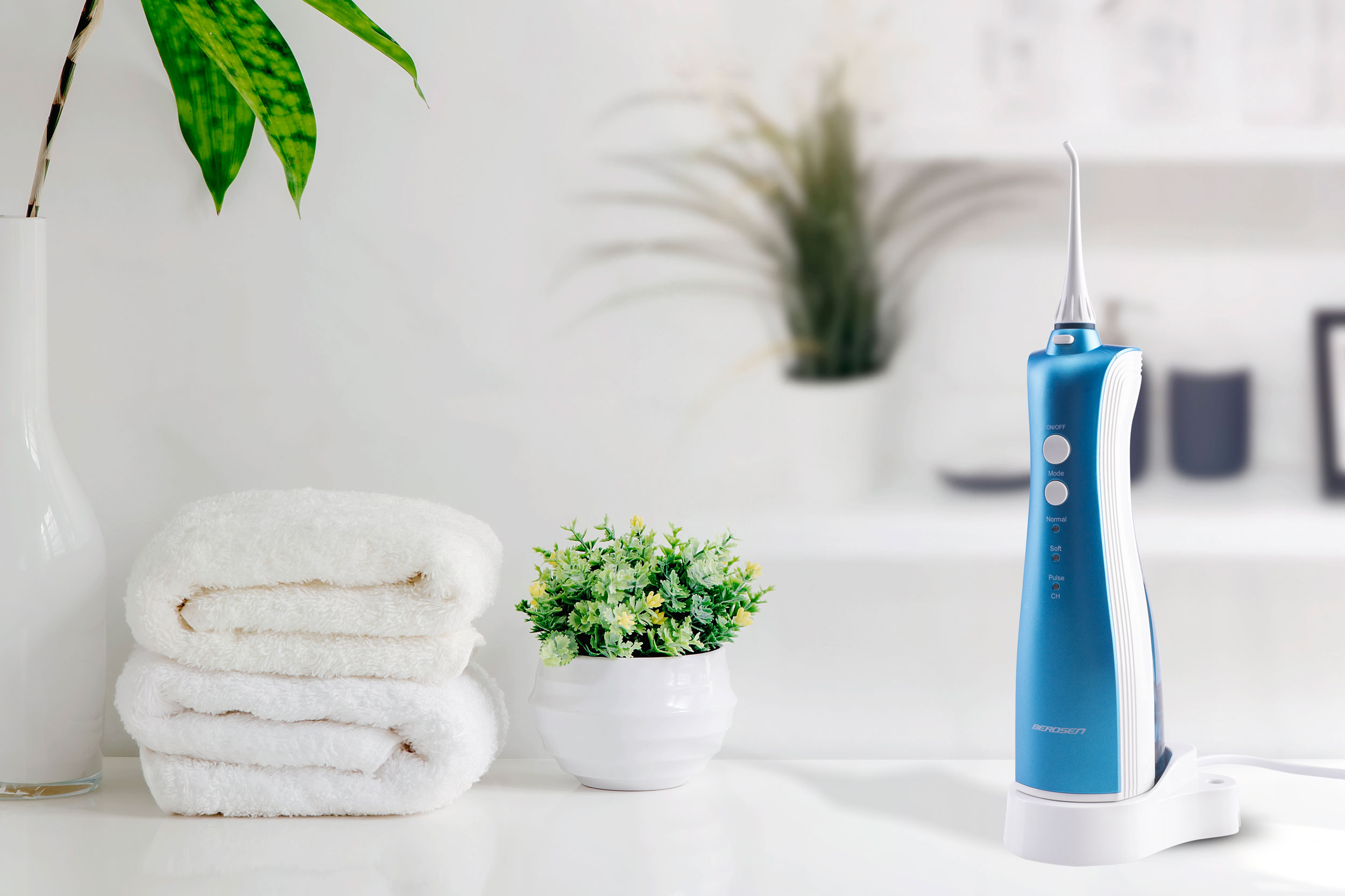 Niebieski i biały irygator na półce z ręcznikami i roślinami. Tło jest rozmyte.