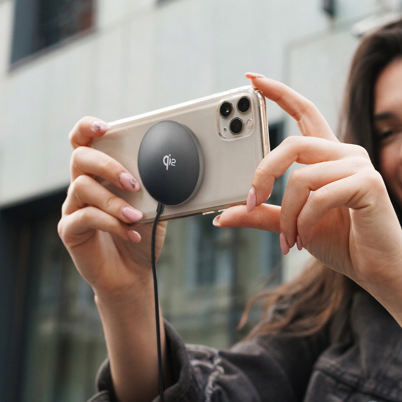 Osoba trzyma telefon z dołączoną okrągłą, czarną ładowarką Qi.