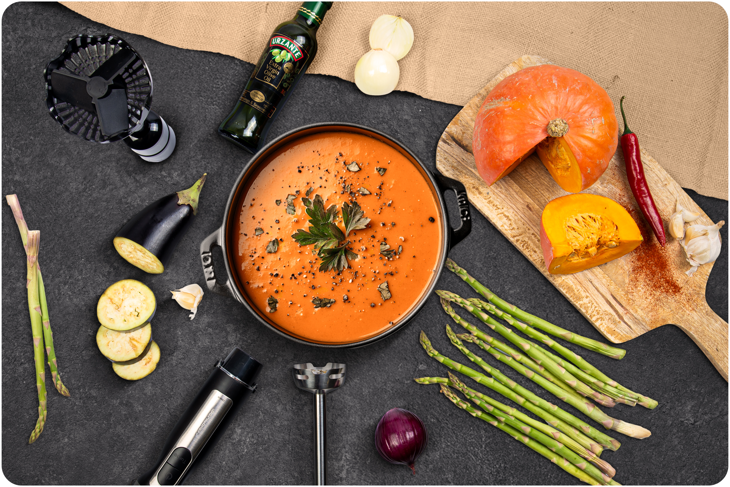 Widok z góry składników i garnka z zupą: dynia, bakłażan, szparagi i oliwa z oliwek.