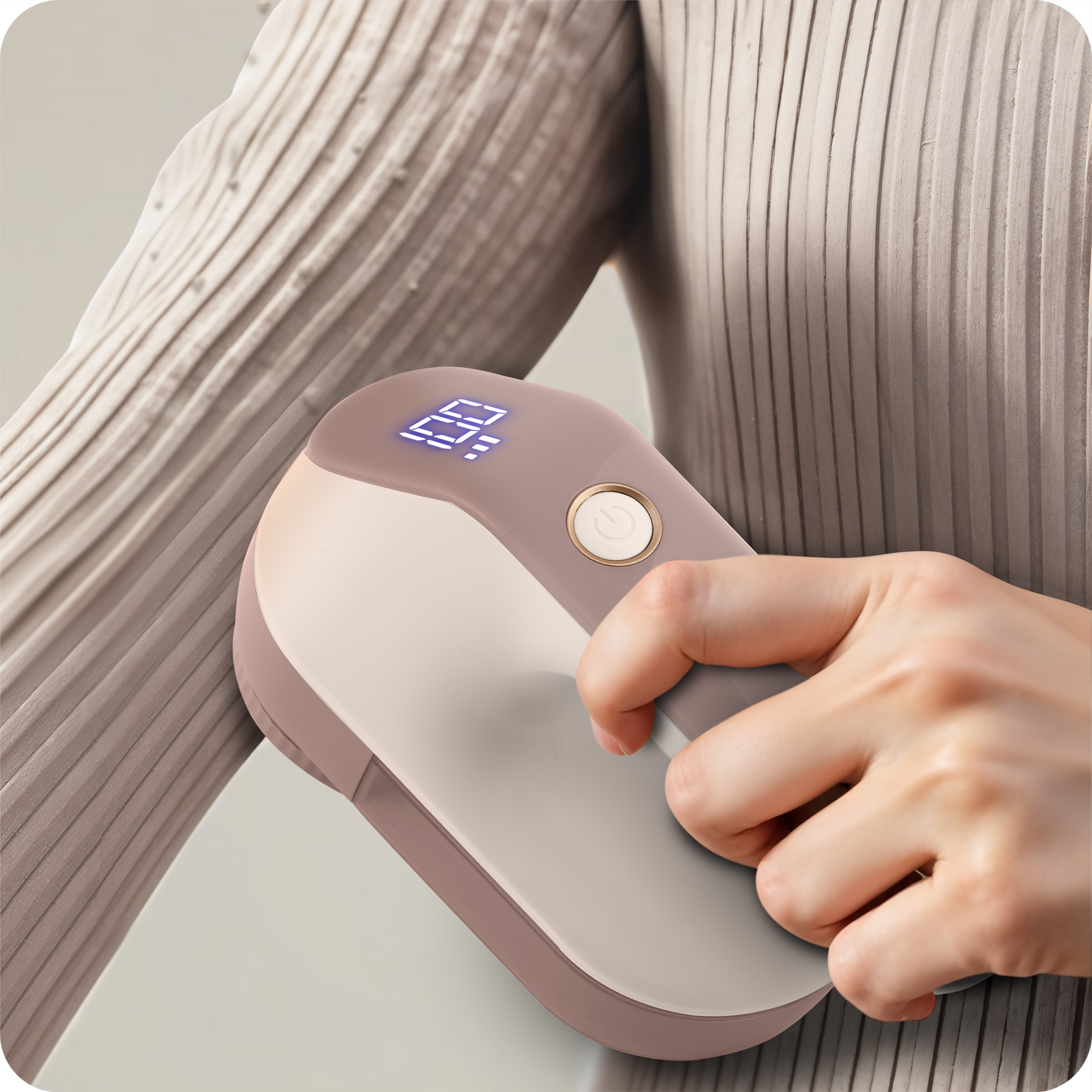 Ręka używająca różowo-białej golarki do tkanin na rękawie jasnobeżowego swetra.