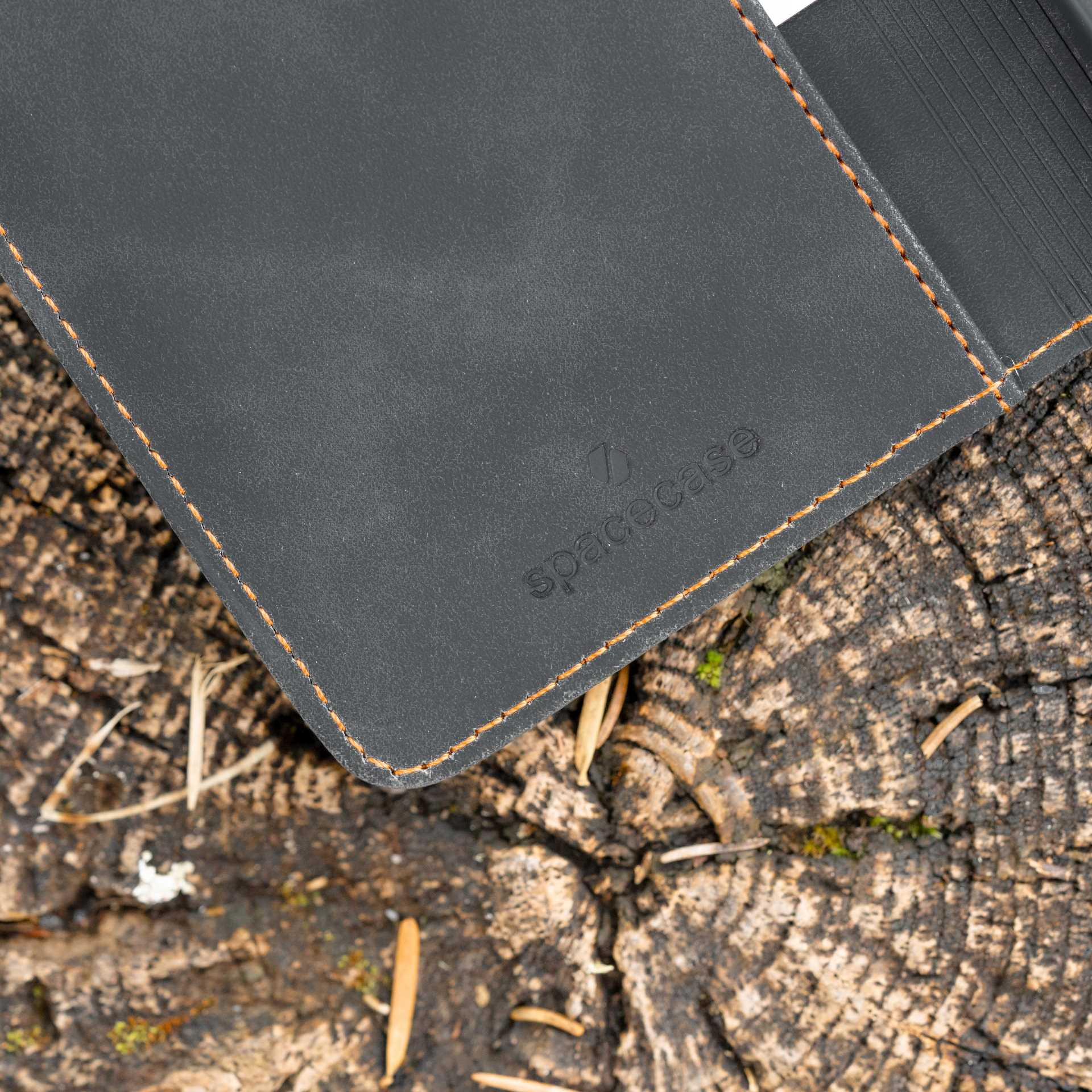 Zbliżenie na ciemnoszare etui na telefon z pomarańczowymi szwami na drewnianej powierzchni. Widoczna nazwa marki.