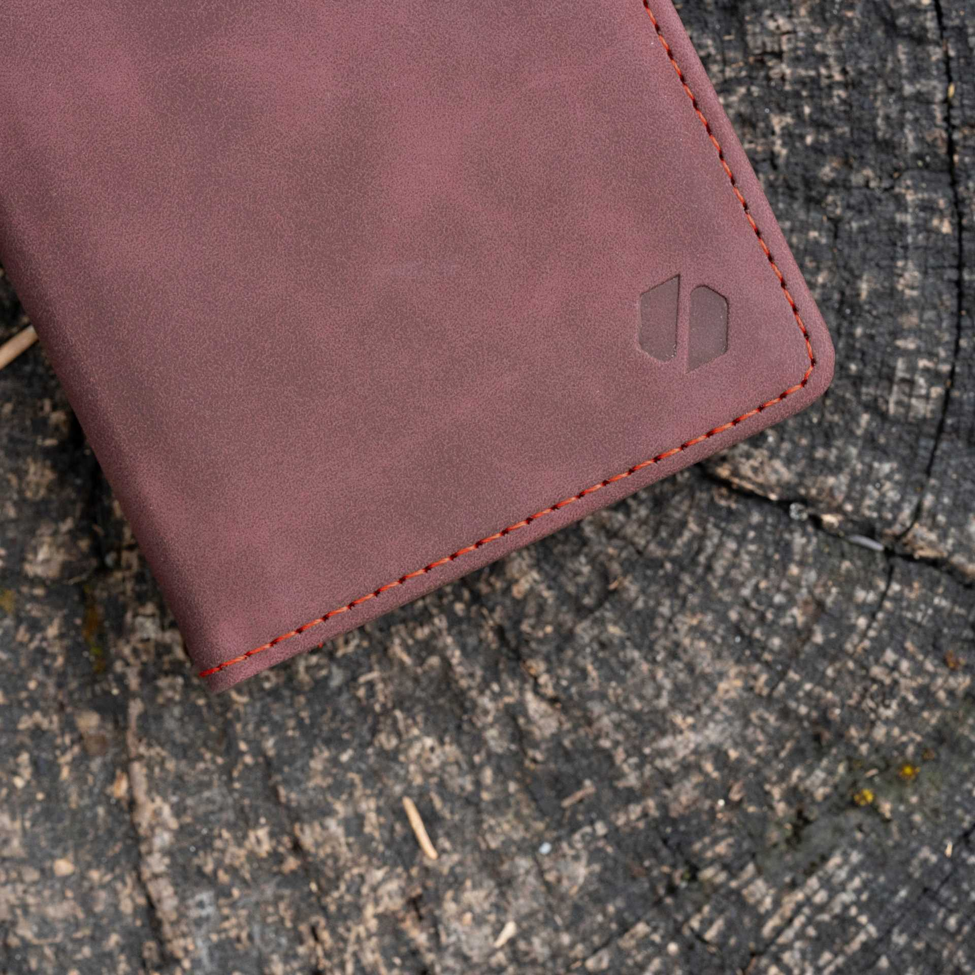 Zbliżenie na bordowe skórzane etui na drewnianej powierzchni. Widoczne czerwone szwy.