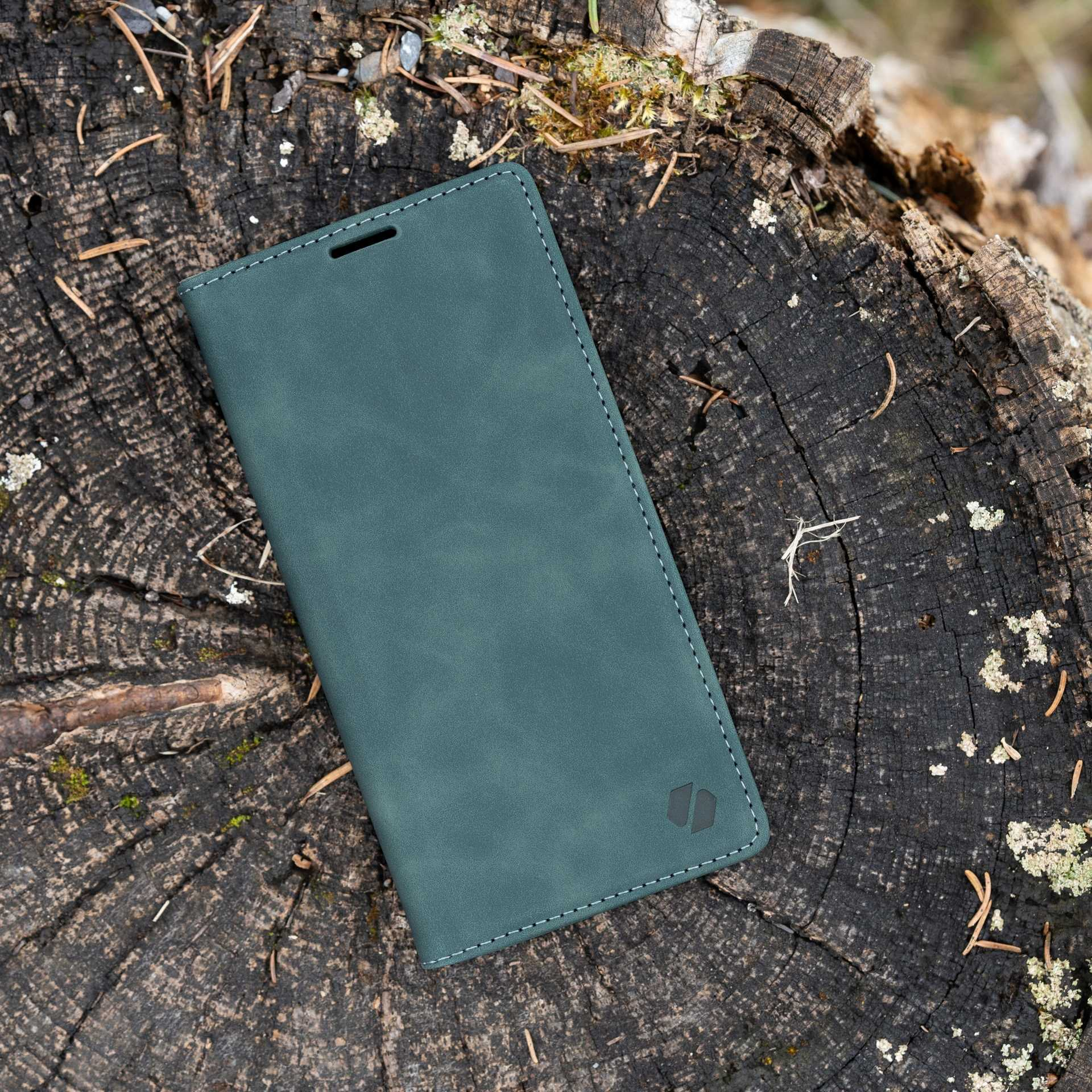 Zielone etui na telefon na pniu drzewa. Etui jest zamknięte. Tłem jest pień drzewa.